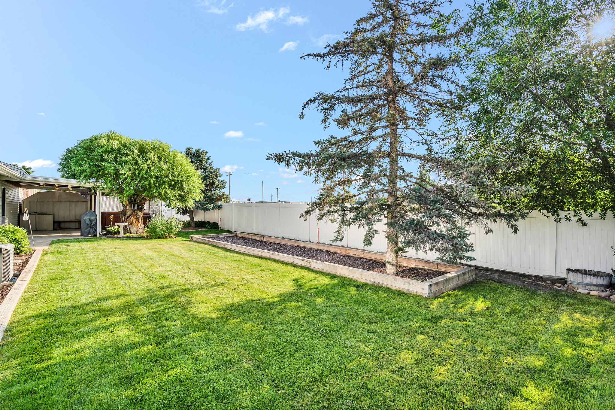 Expansive rear yard featuring a manicured lawn, established landscaping, privacy fencing, a concrete planter box, and a covered patio area