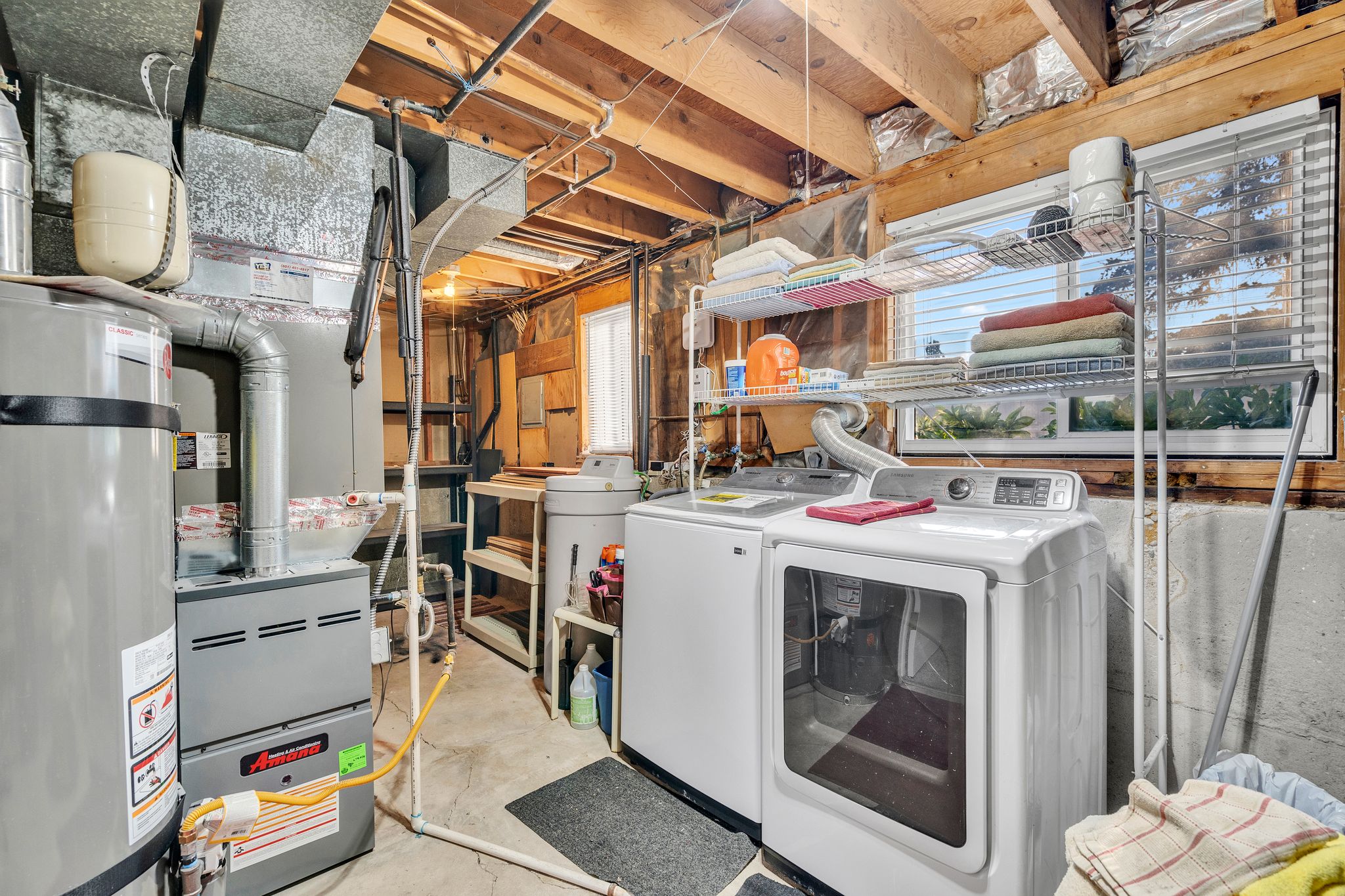 Dedicated utility area featuring a water heater, furnace, exposed ceiling joists, and a horizontal window