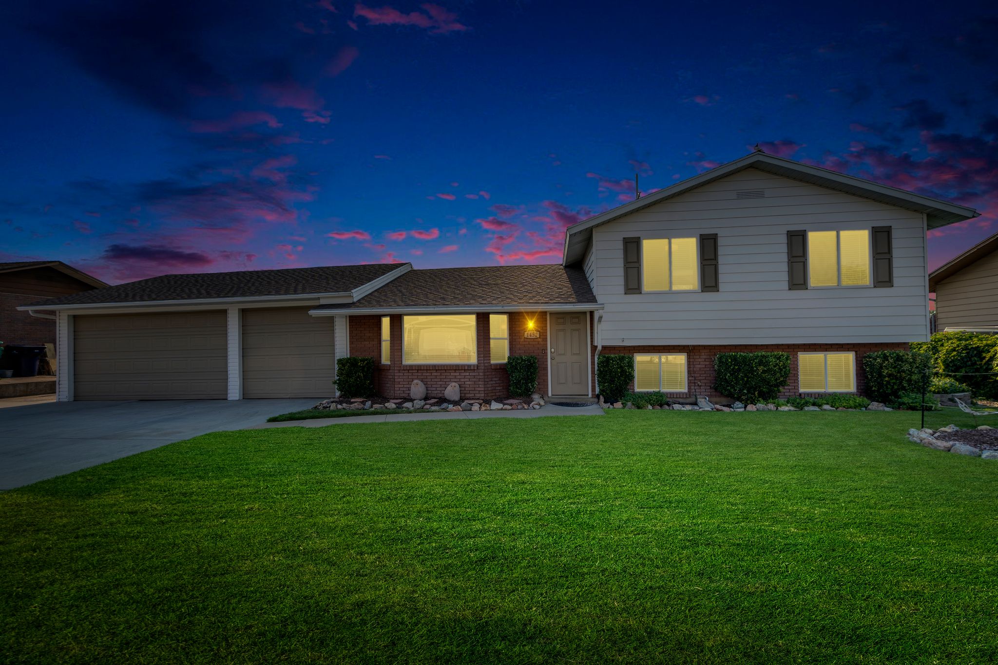 Traditional style exterior featuring a two-car garage, brick accents, and a verdant lawn