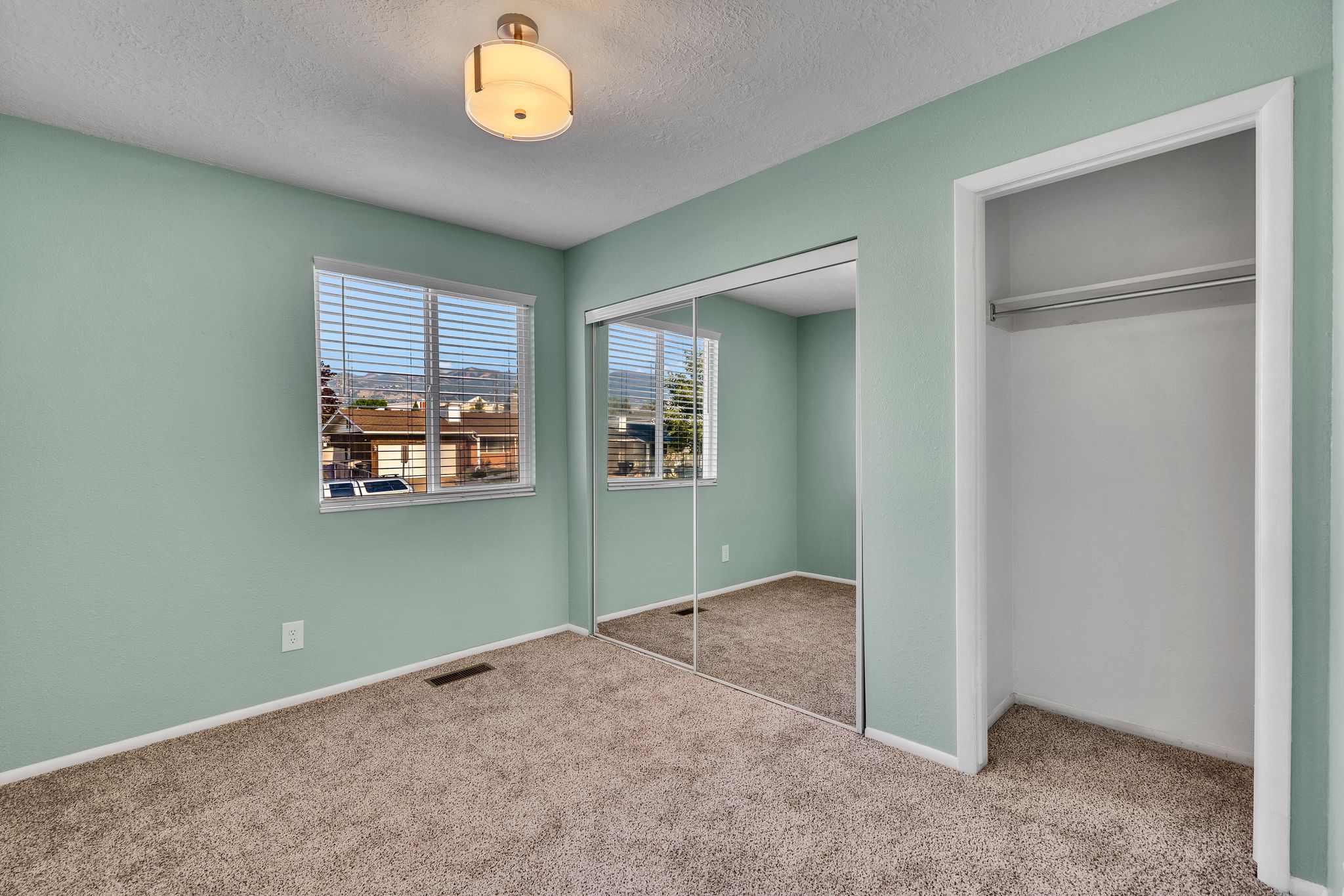 Carpeted room with a ceiling-mounted light fixture, louvered window blinds, mirrored closet doors, and an additional open closet space