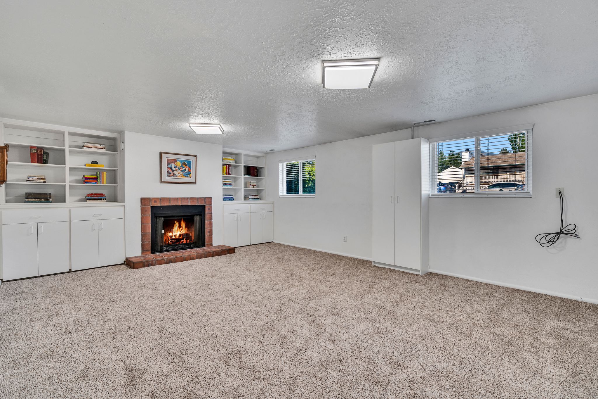 Interior room featuring a brick-surround fireplace, built-in shelving, white cabinetry, and carpeted flooring