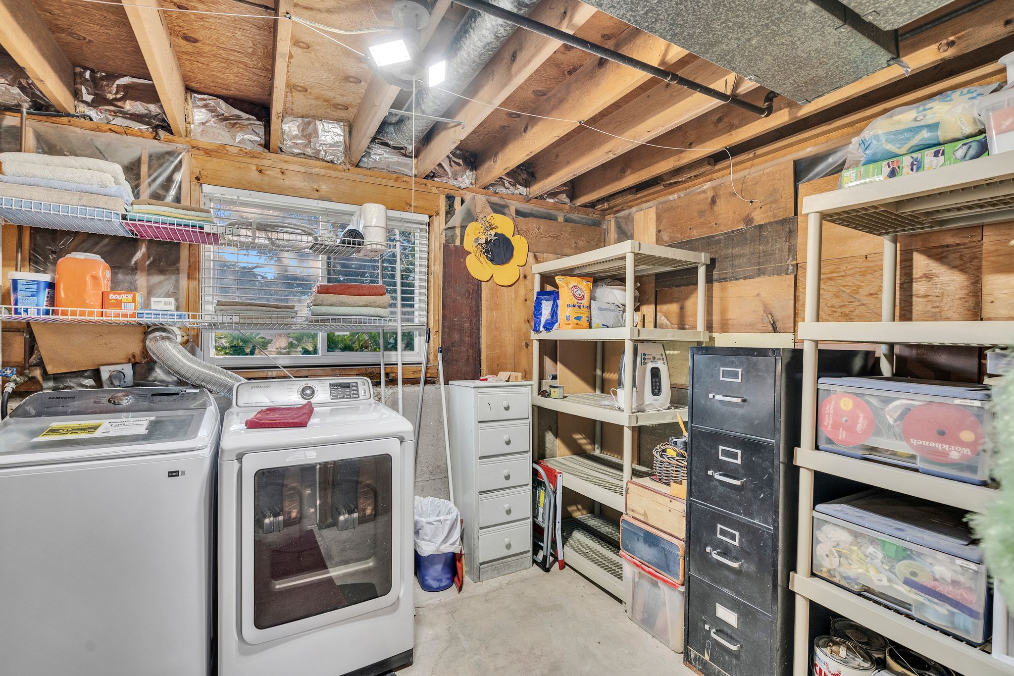 Dedicated laundry area featuring a window, exposed ceiling joists, and concrete flooring