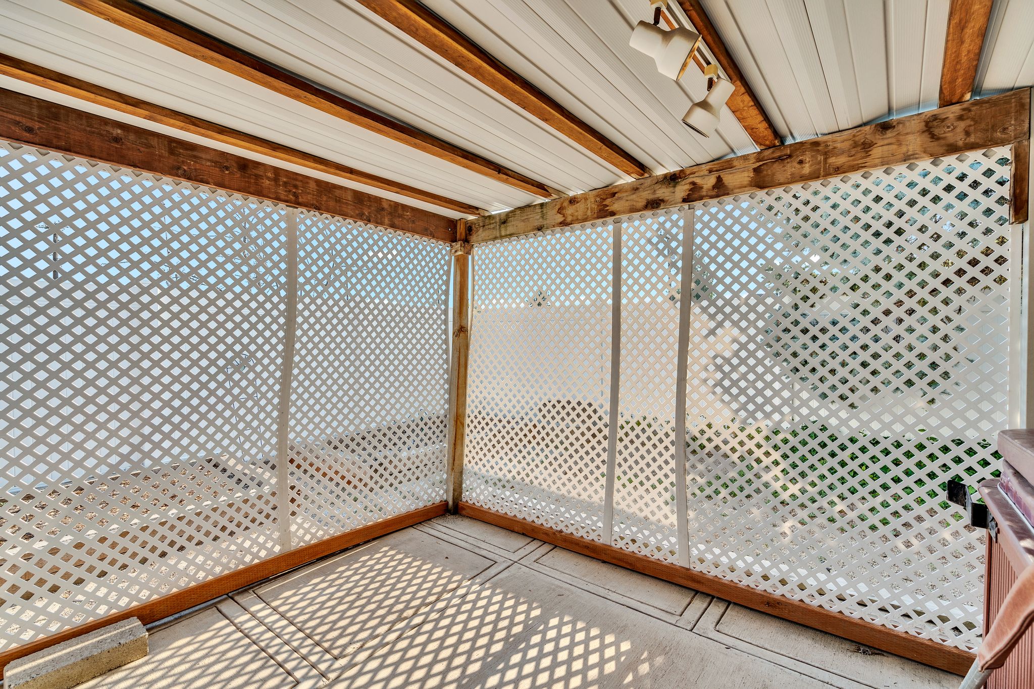 Covered patio featuring a slatted white ceiling, exposed wood beams, and lattice privacy screens