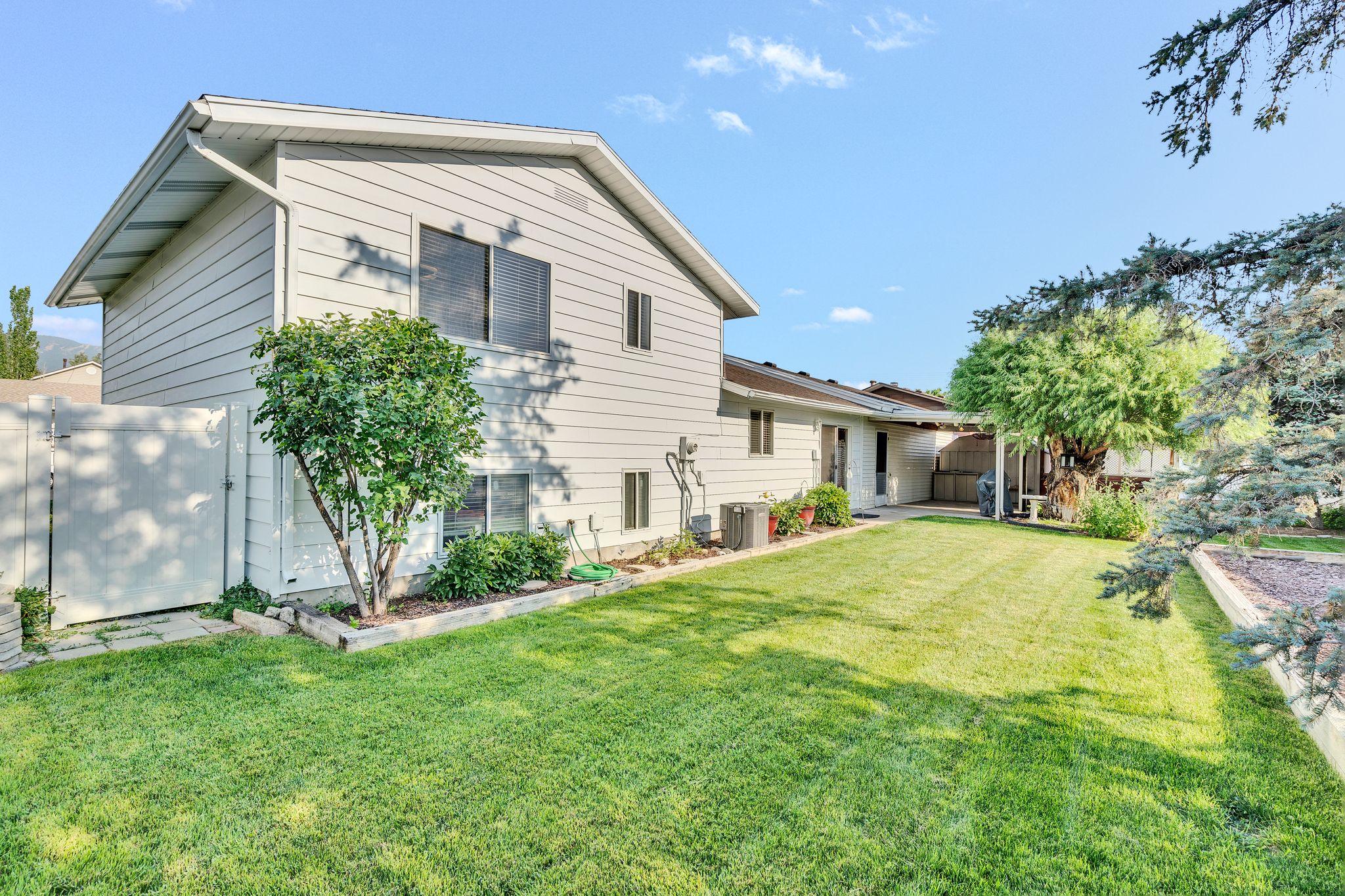 Expansive backyard featuring a manicured lawn, mature trees, and a wooden privacy fence