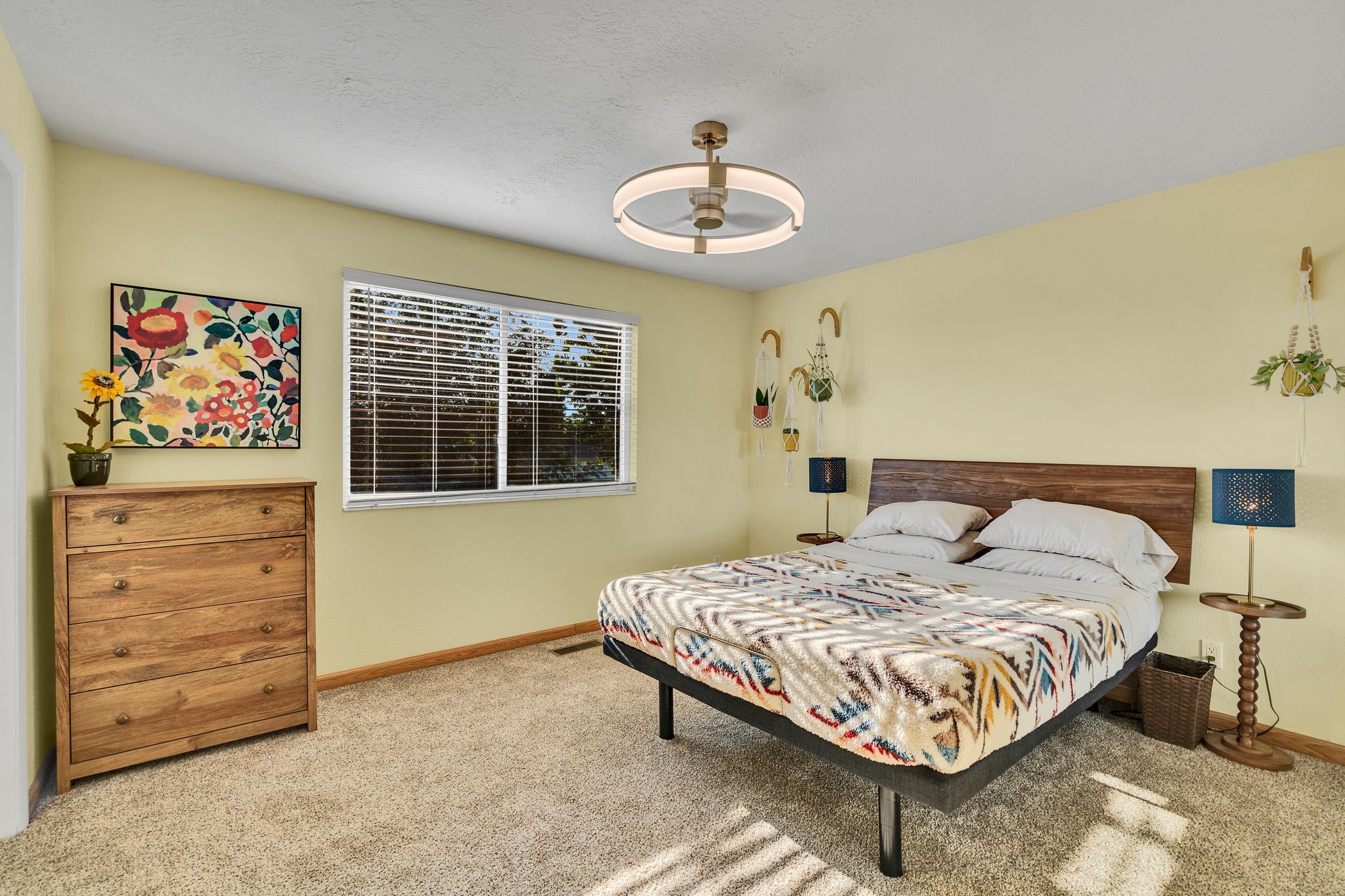 Carpeted bedroom featuring a large window with horizontal blinds, a ceiling-mounted fan with integrated lighting, and light-toned walls