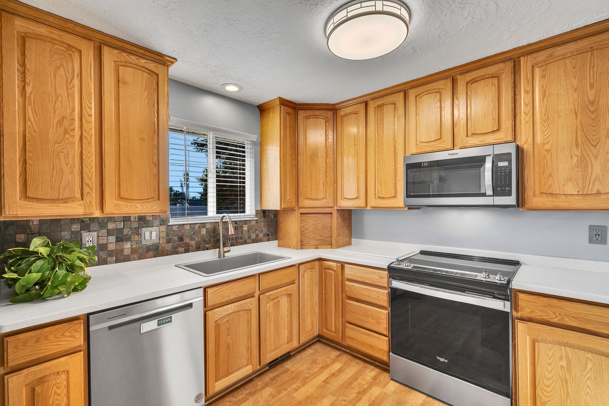 Kitchen featuring wood-finish cabinetry, solid surface countertops, stainless steel appliances, and a mosaic tile backsplash