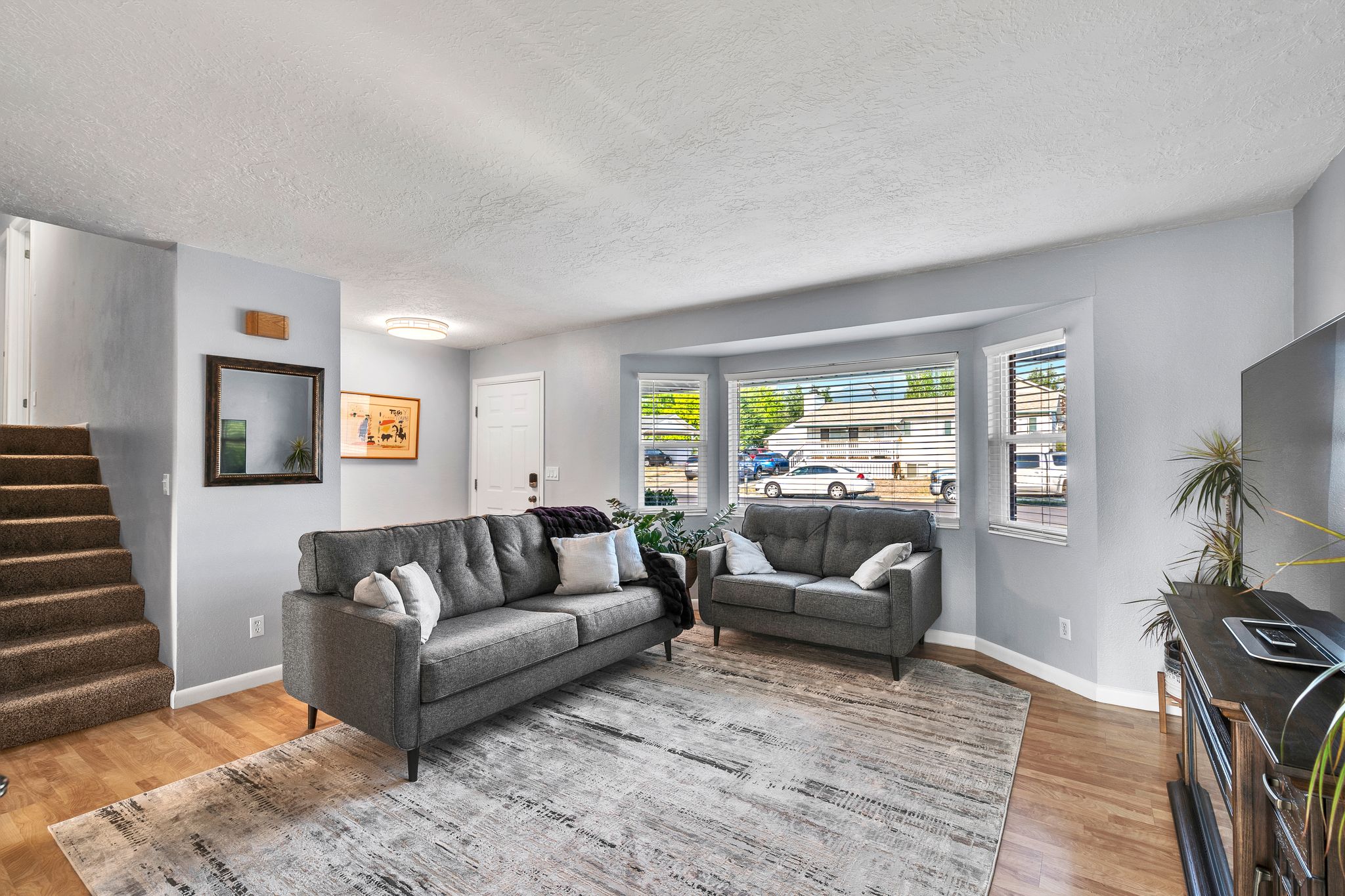 Living area featuring wood-finish flooring, light gray wall paint, and a bay window with blinds