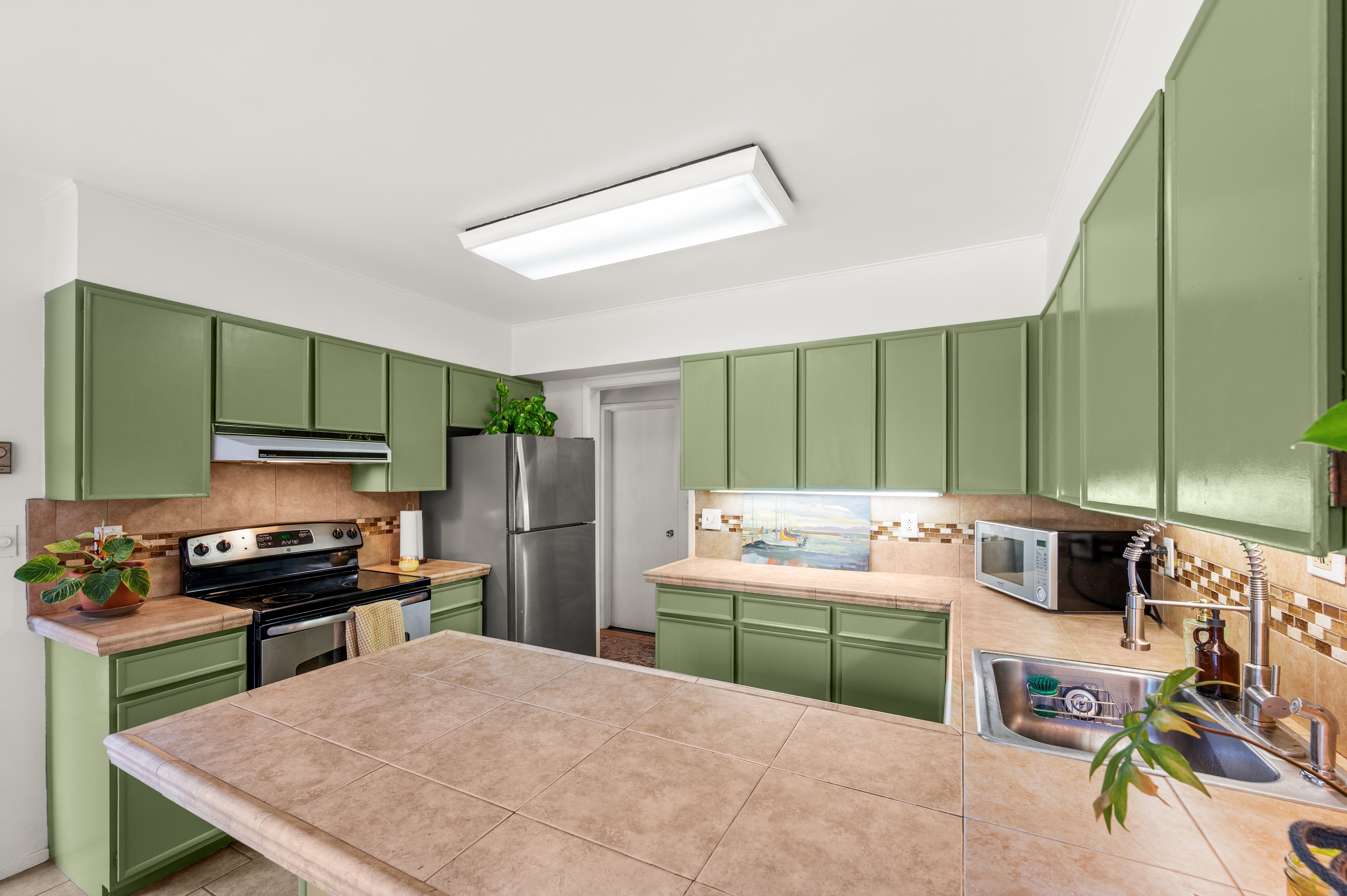 Kitchen featuring extensive green cabinetry, tile countertops, a tile backsplash, and stainless steel appliances