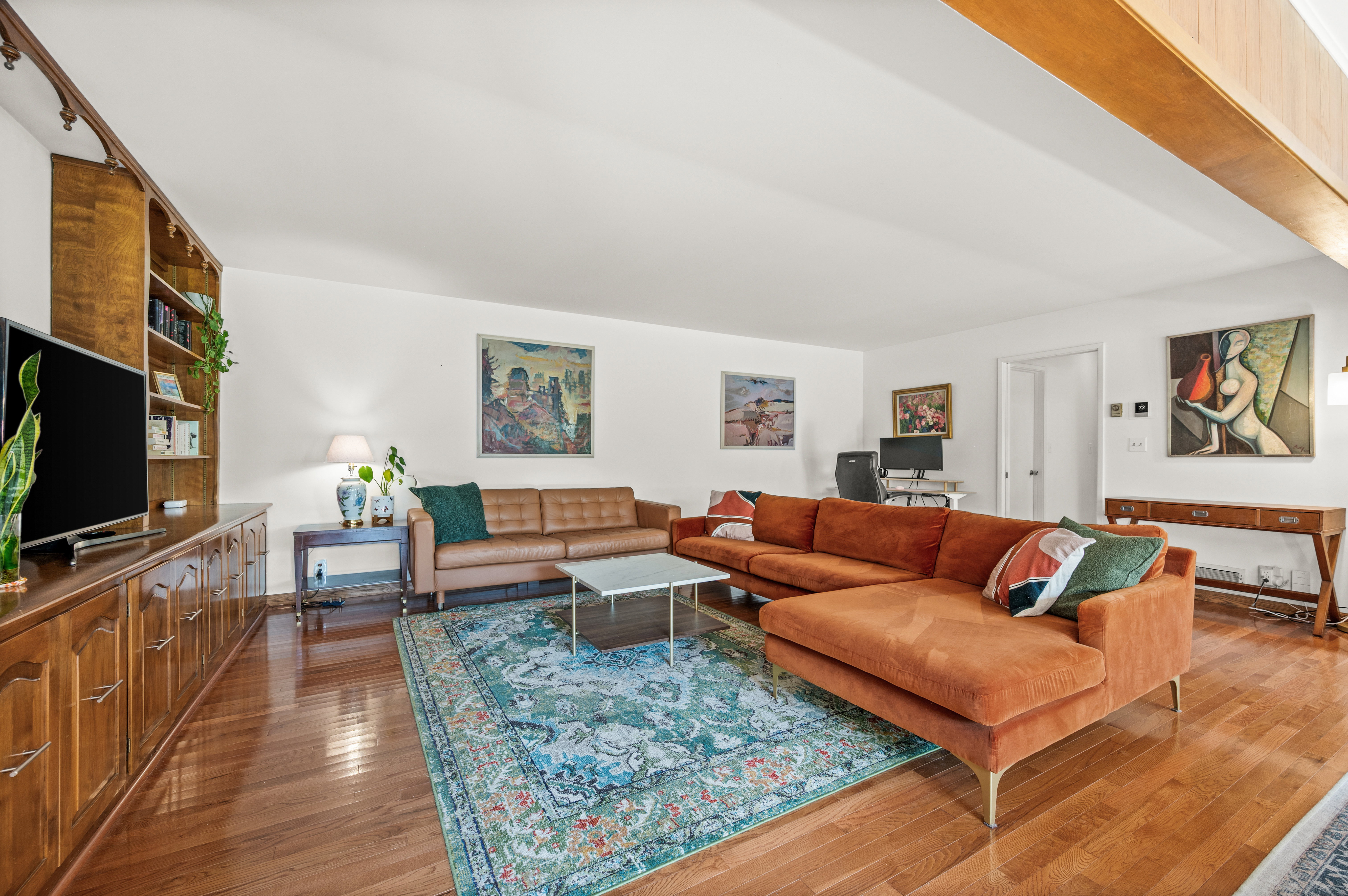 Spacious living area featuring wood-finish flooring, a built-in shelving unit with lower cabinetry, and a large area rug