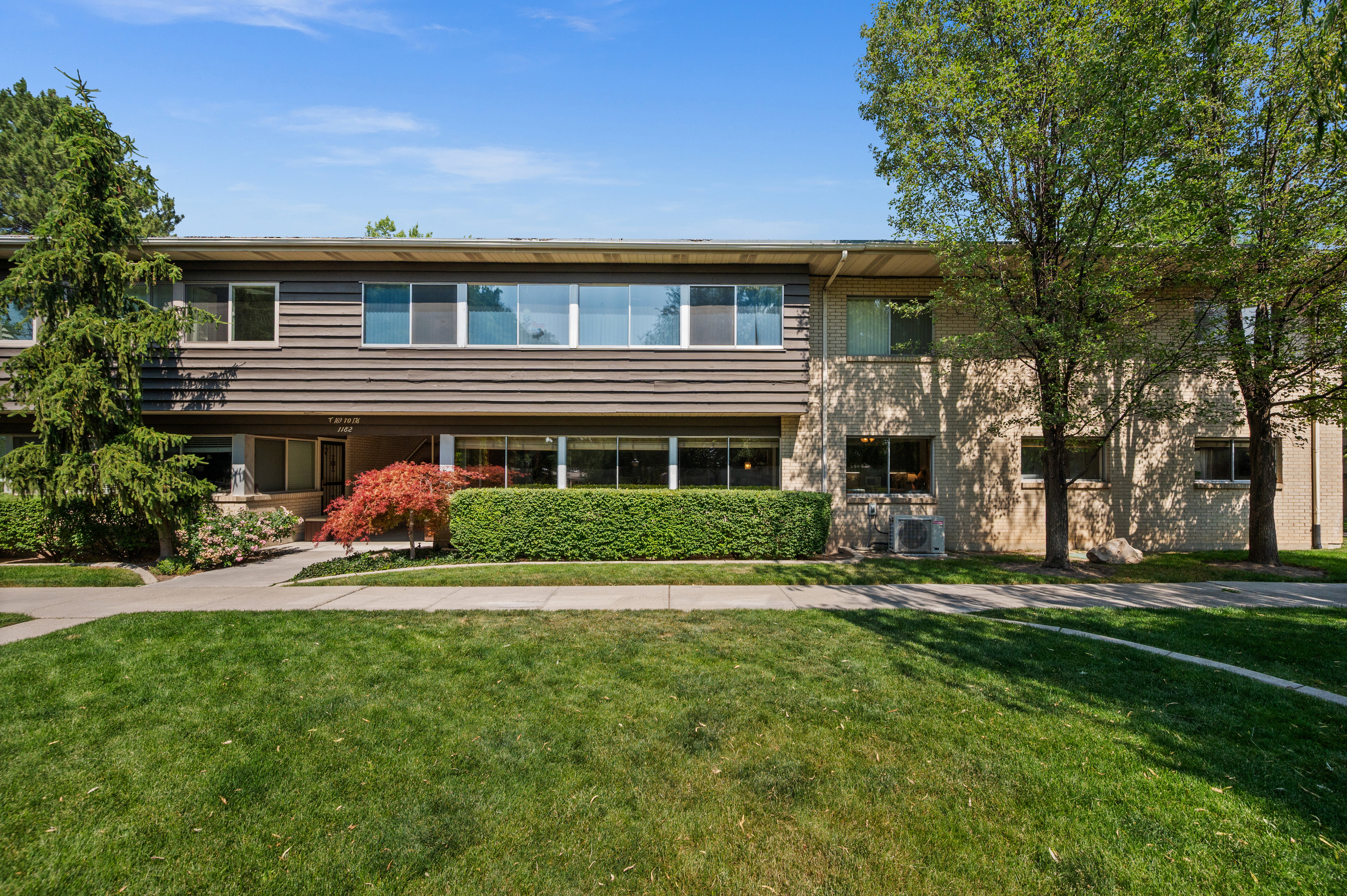 Two-story building featuring horizontal siding and brick facades, multiple large windows, mature landscaping, and a manicured lawn