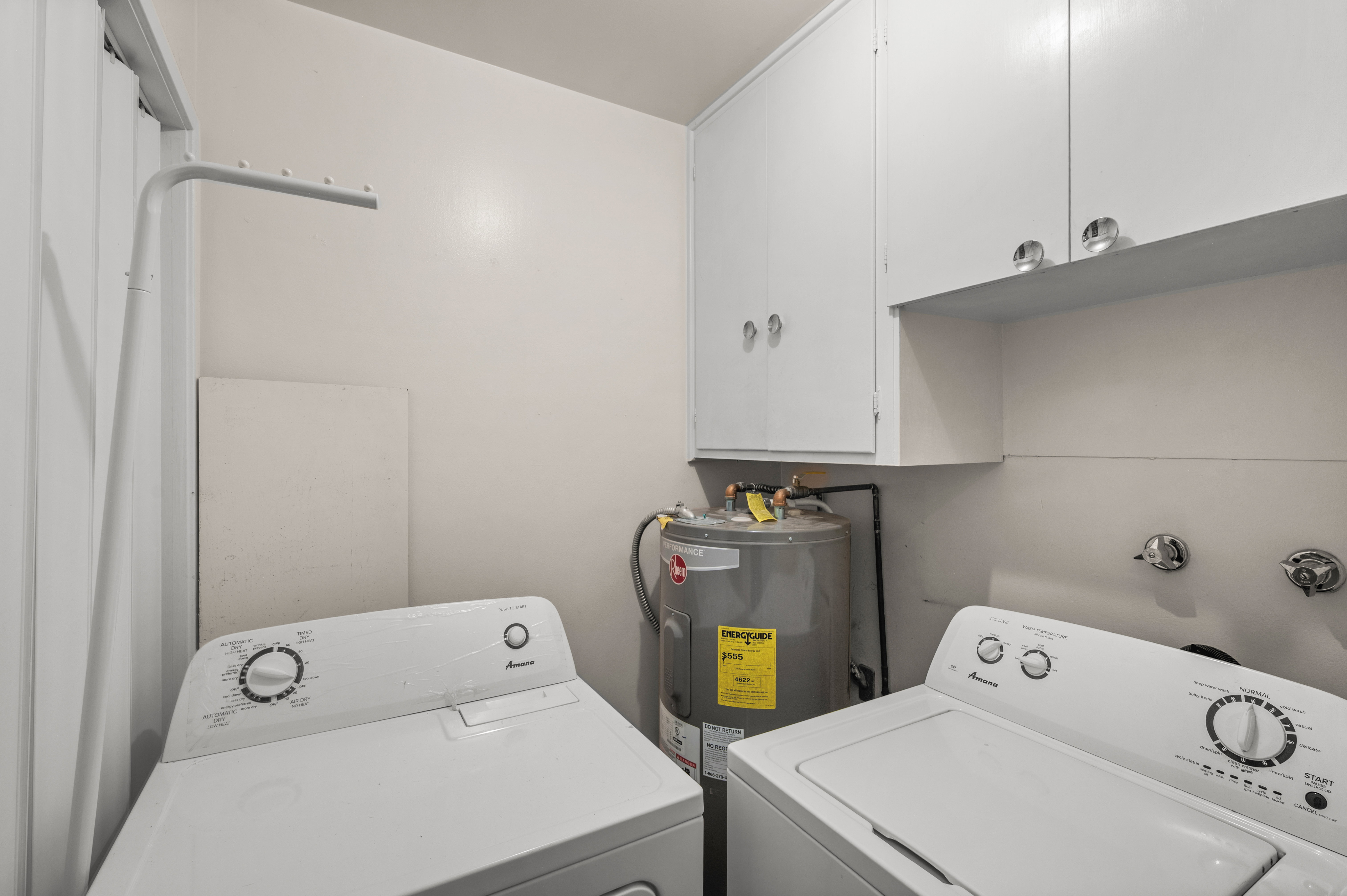 Dedicated laundry area featuring a water heater, upper cabinetry, and a wall-mounted drying rack