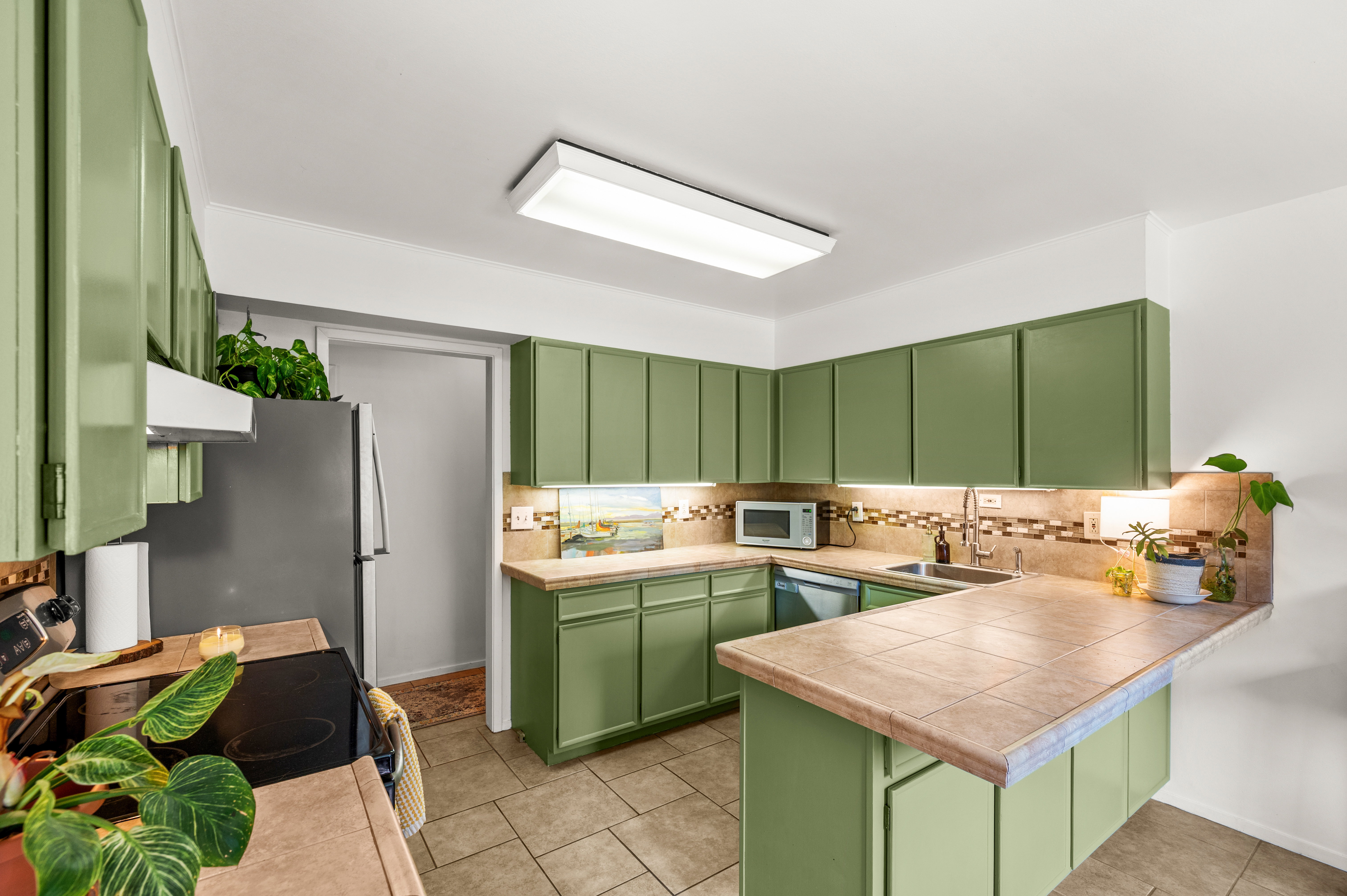 Kitchen featuring green cabinetry, tile flooring, built-in stainless steel appliances, a tile backsplash, and a breakfast bar with a tile countertop