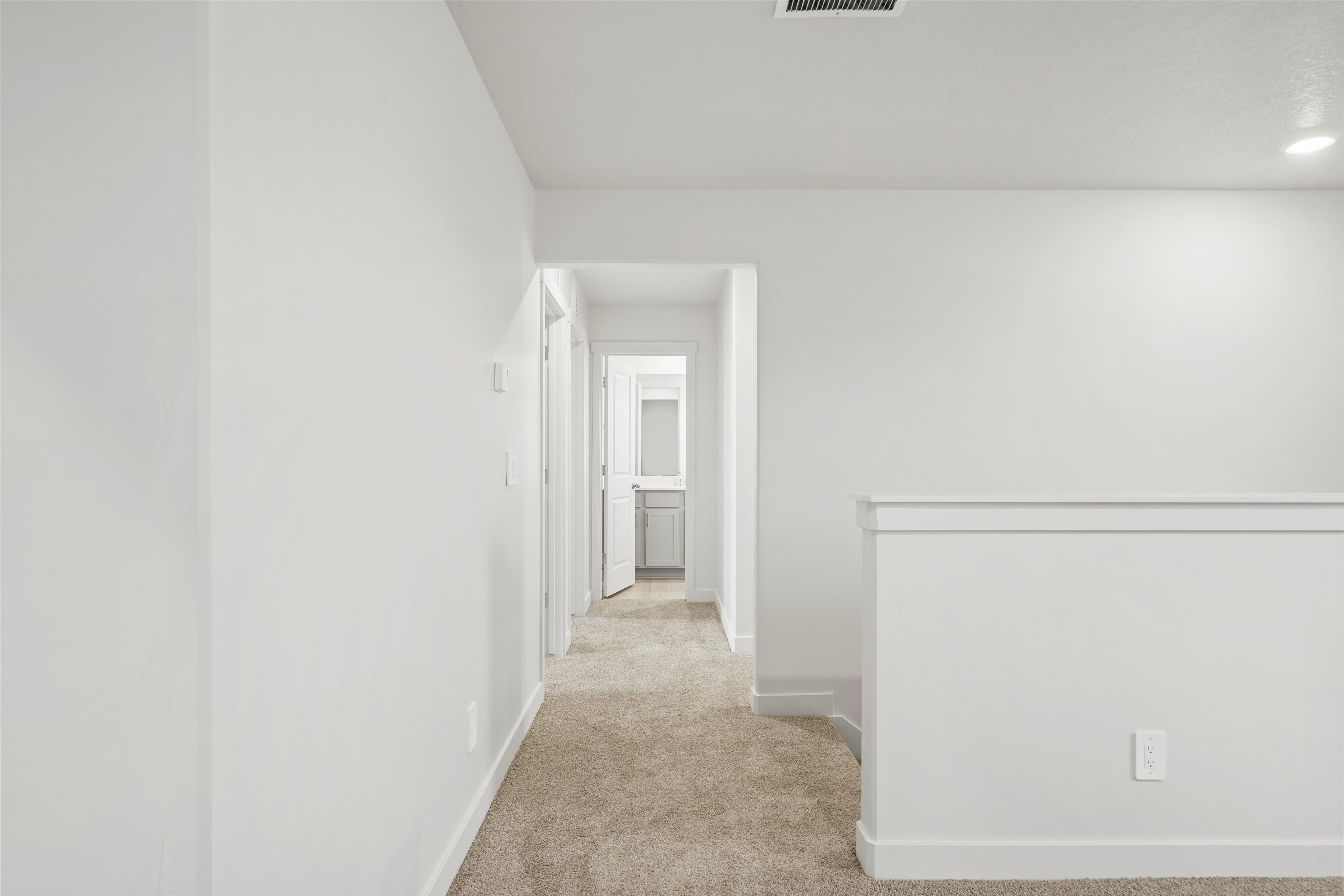 **DISCLAIMER** Interior package may vary. Carpeted hallway with white walls and trim, featuring recessed lighting and a visible doorway leading to an additional space