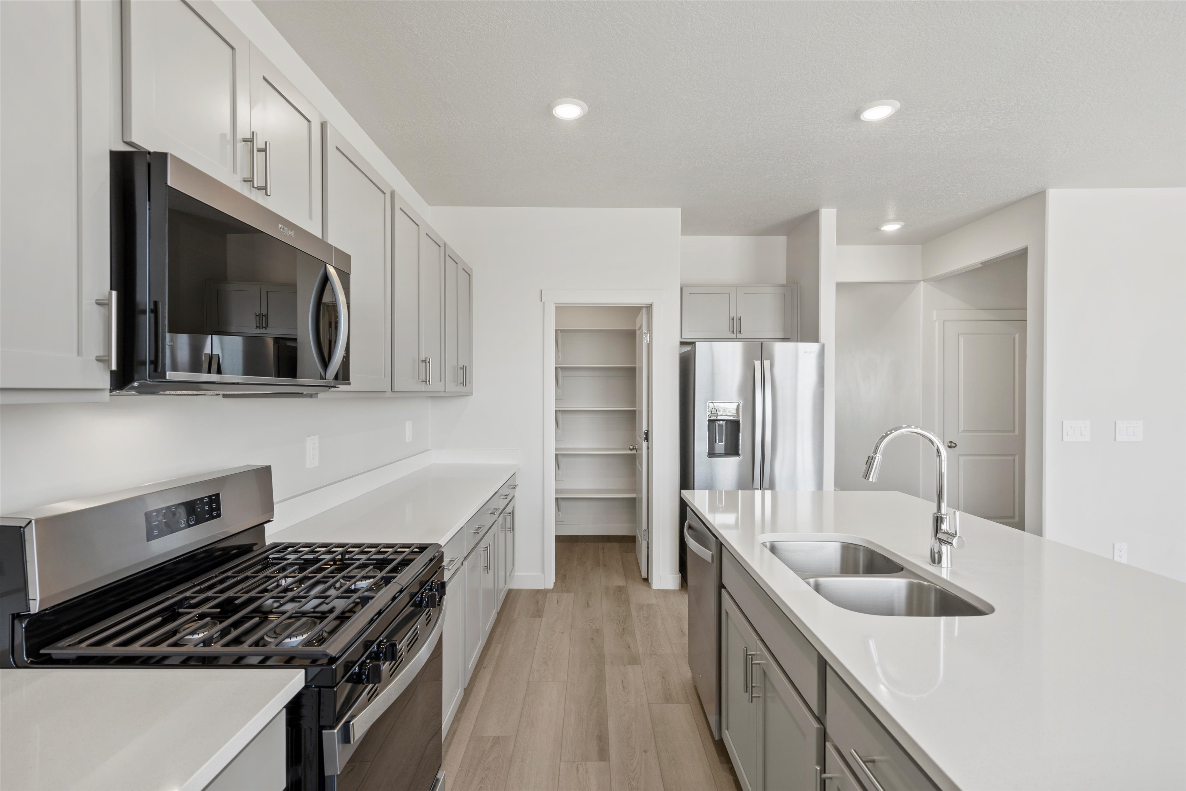 **DISCLAIMER** Interior package may vary. Modern kitchen featuring white countertops, light gray cabinetry, stainless steel appliances, and wood-finish flooring