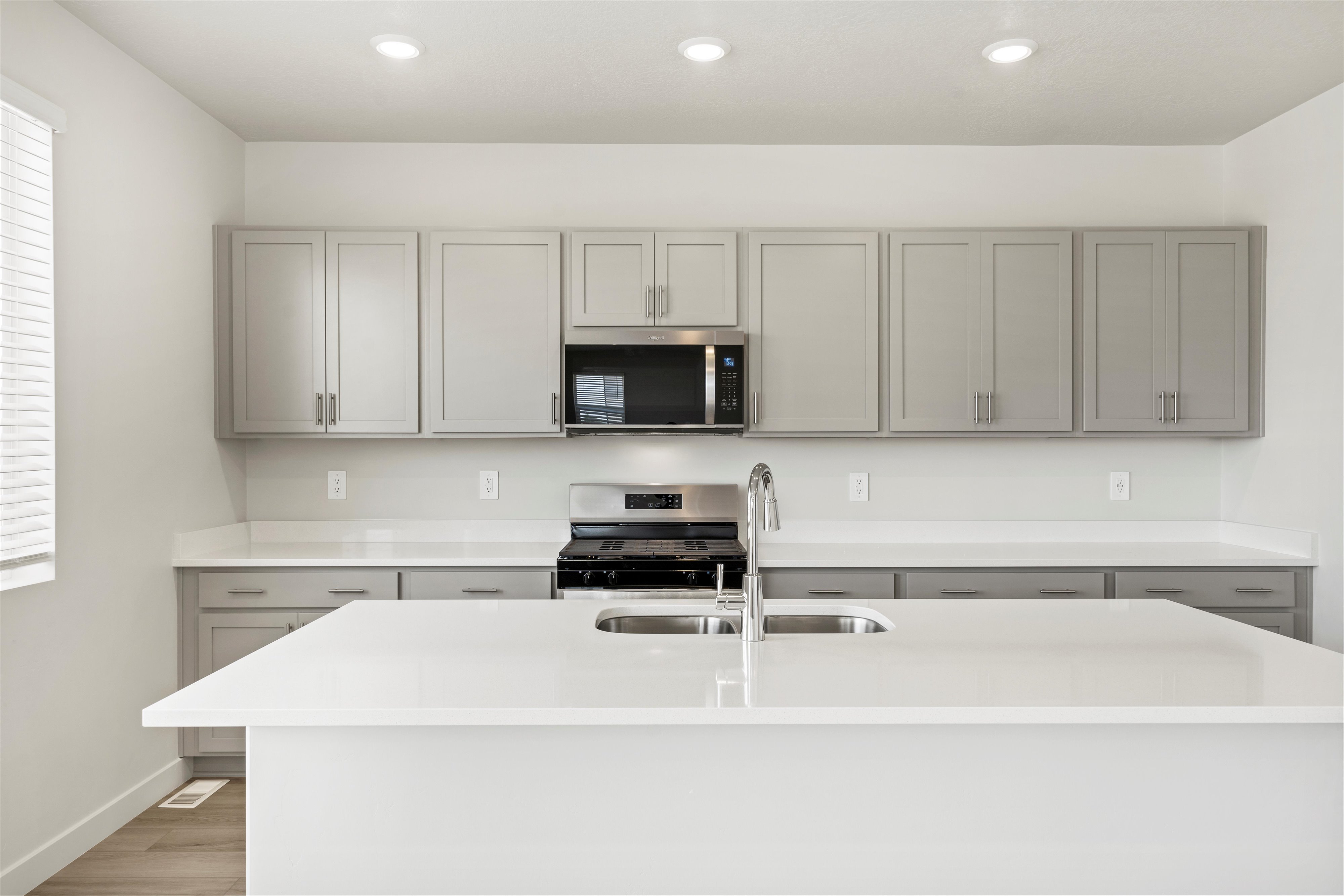 **DISCLAIMER** Interior package may vary. Kitchen featuring a large island with an undermount double-basin sink, light grey shaker cabinetry, white countertops, and a built-in stainless steel microwave