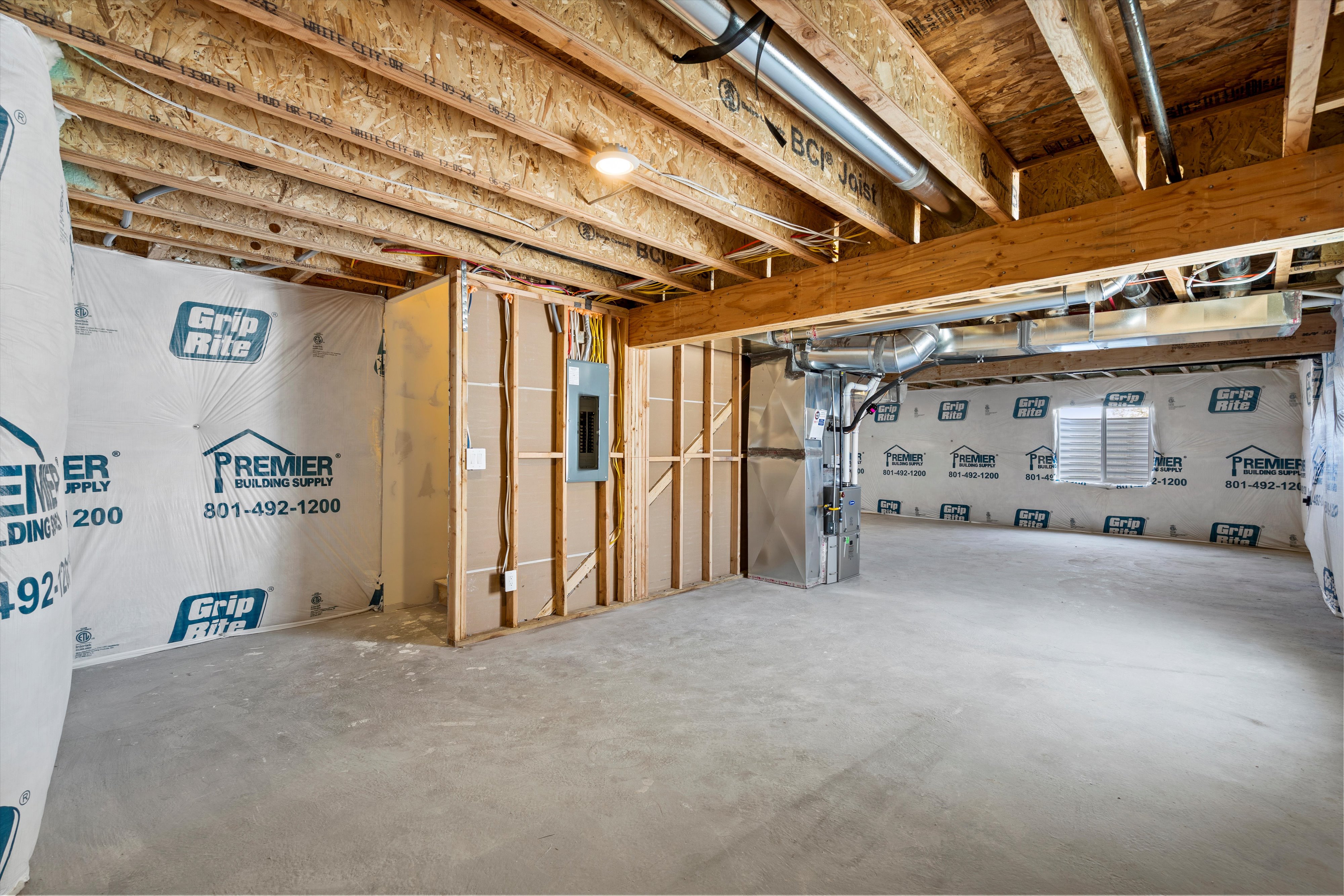 Unfinished basement space featuring exposed wood joists and subflooring, concrete slab, and framed partition walls