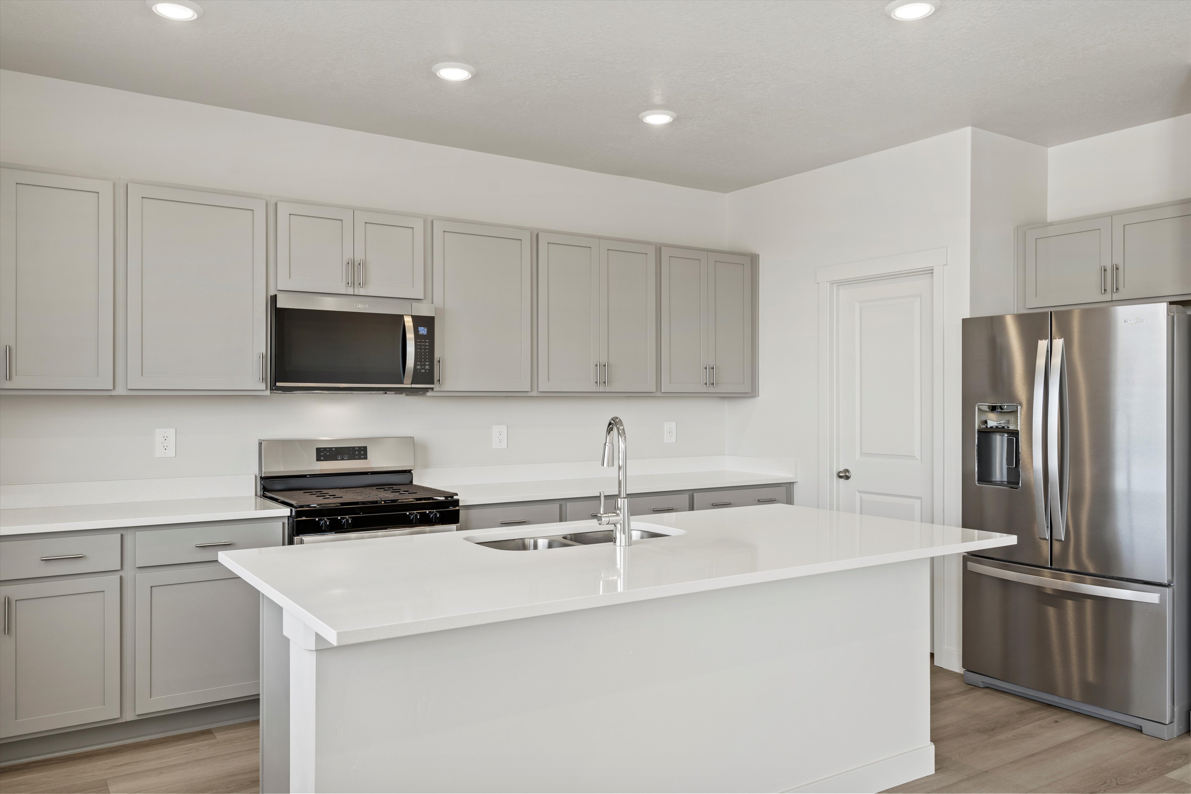 **DISCLAIMER** Interior package may vary. Spacious kitchen featuring an island with an undermount sink, light gray cabinetry, stainless steel appliances, white countertops, and wood-finish flooring