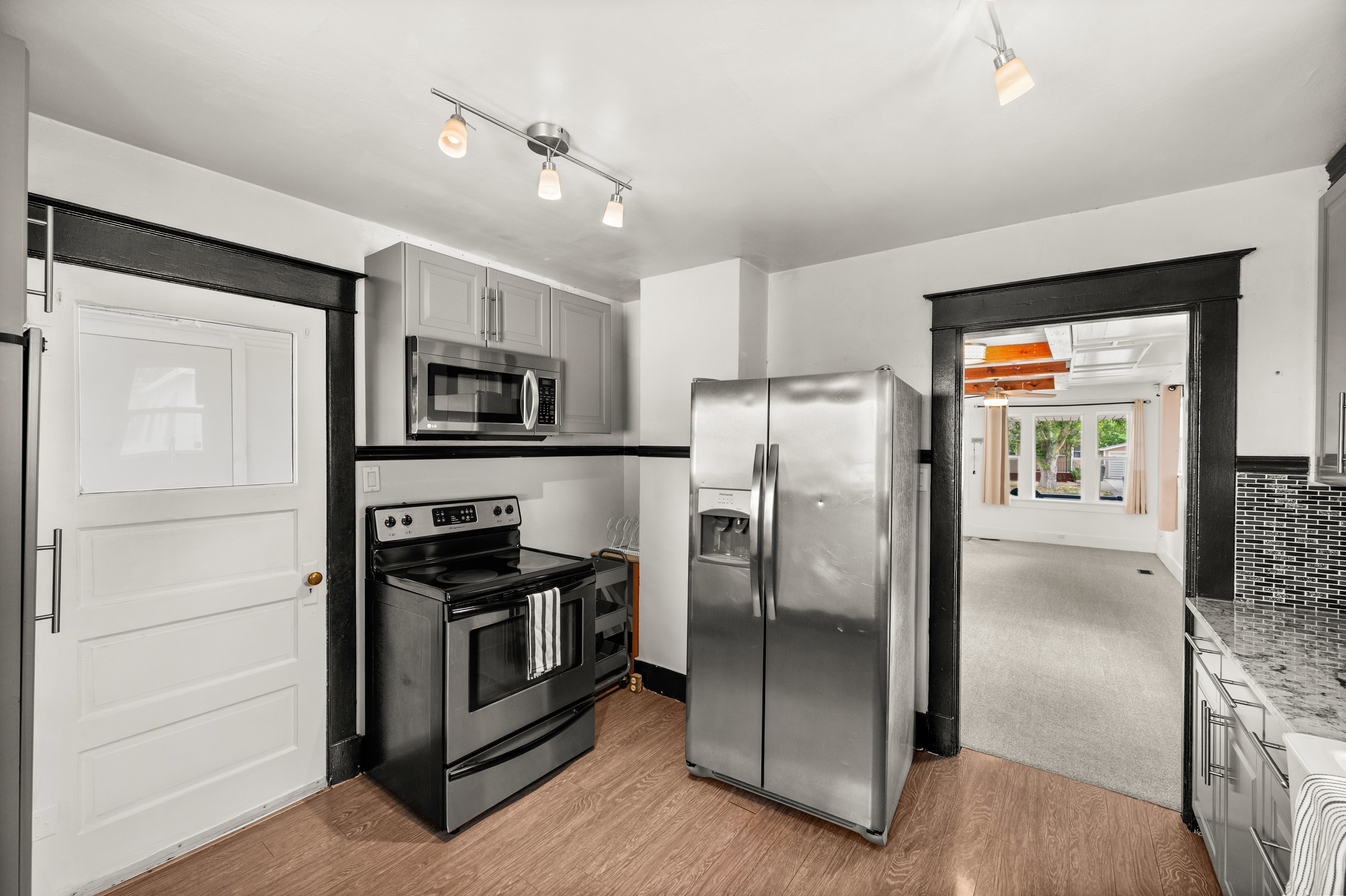 Kitchen featuring wood-finish flooring, stainless steel appliances, gray cabinetry, and granite countertops with a mosaic tile backsplash