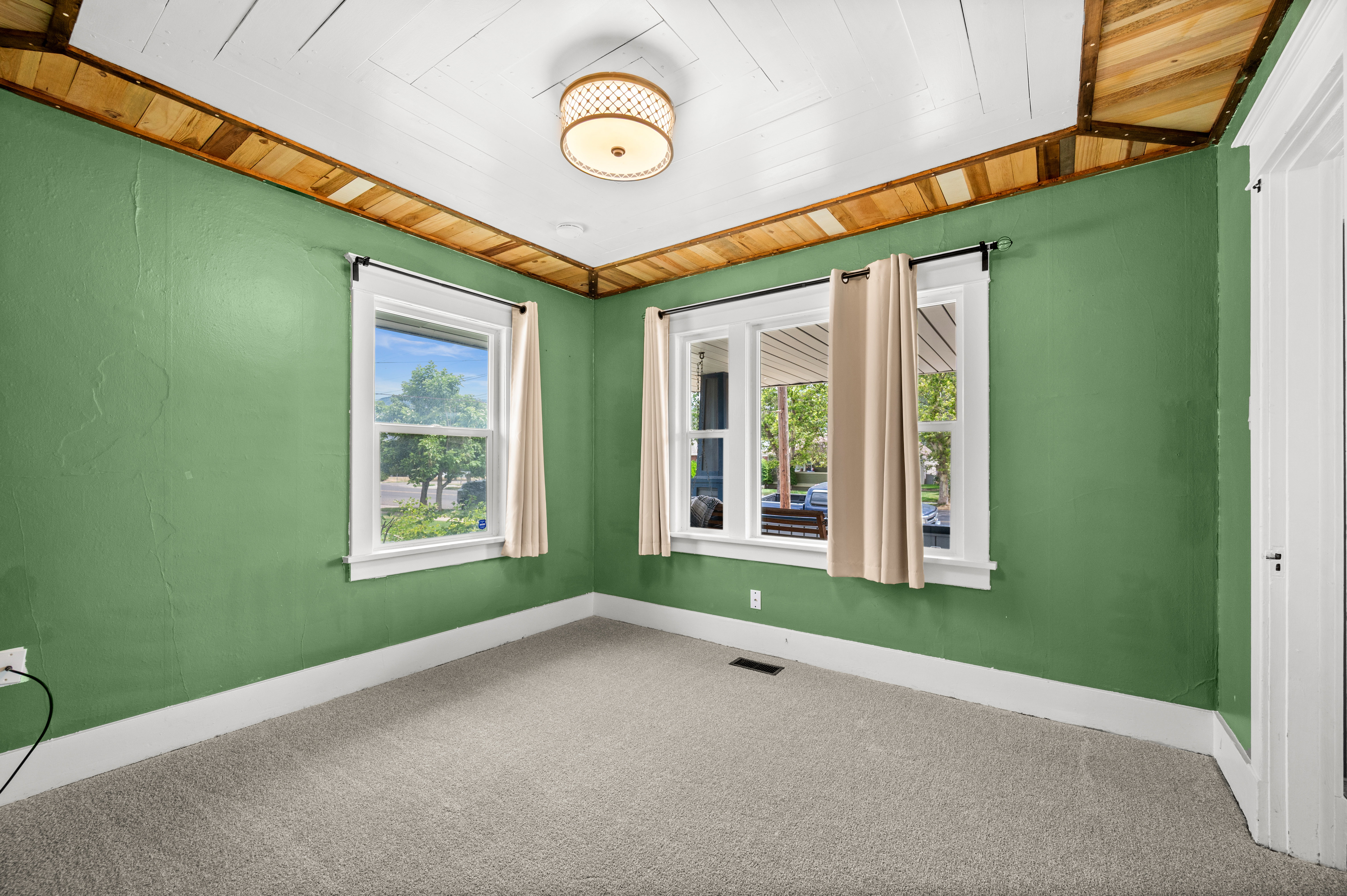 Bright room featuring a paneled ceiling with natural wood accents, two windows with white trim, green textured walls, and light-colored carpeting