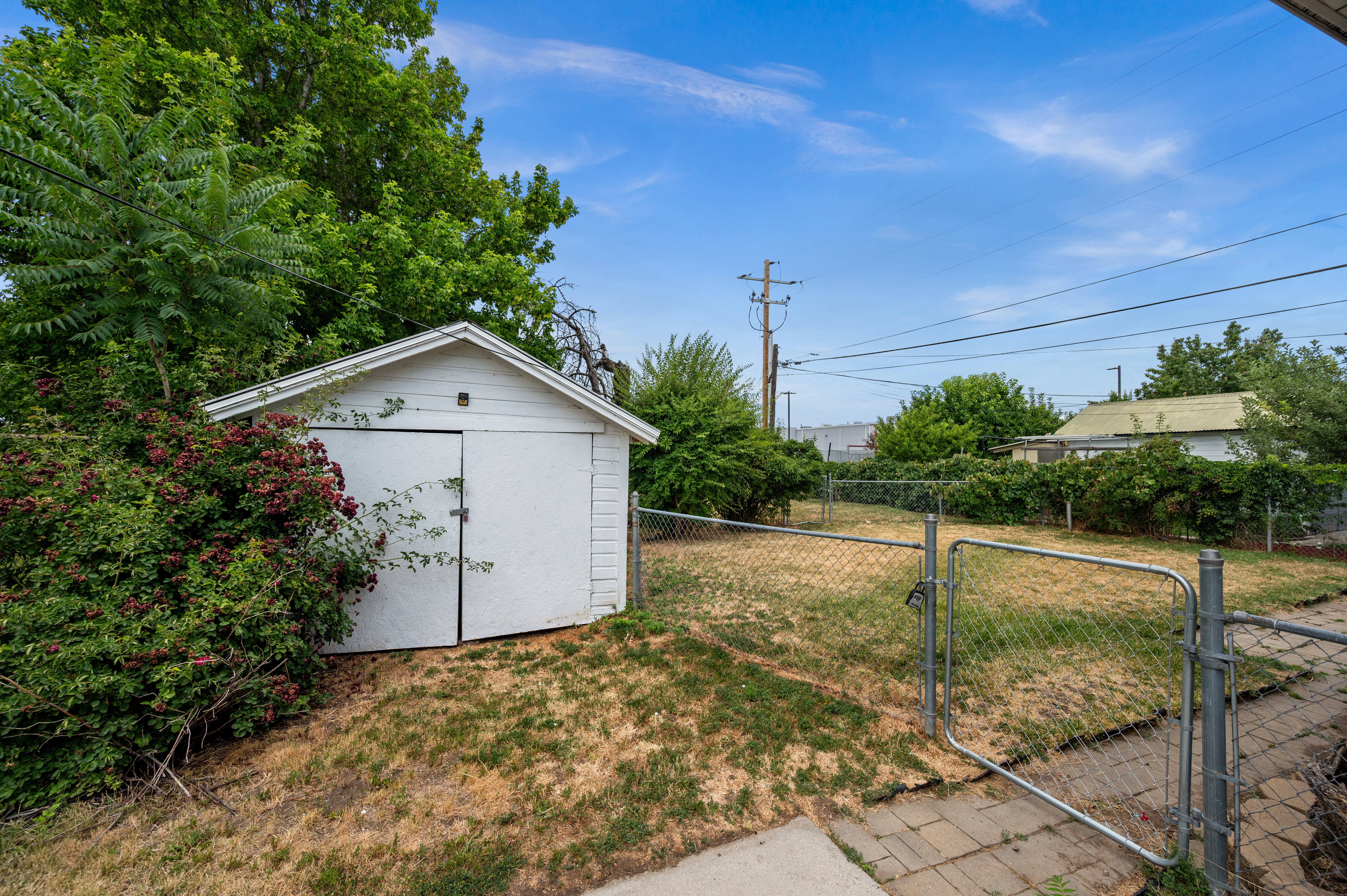 Detached storage shed with white siding and double barn doors, surrounded by mature greenery