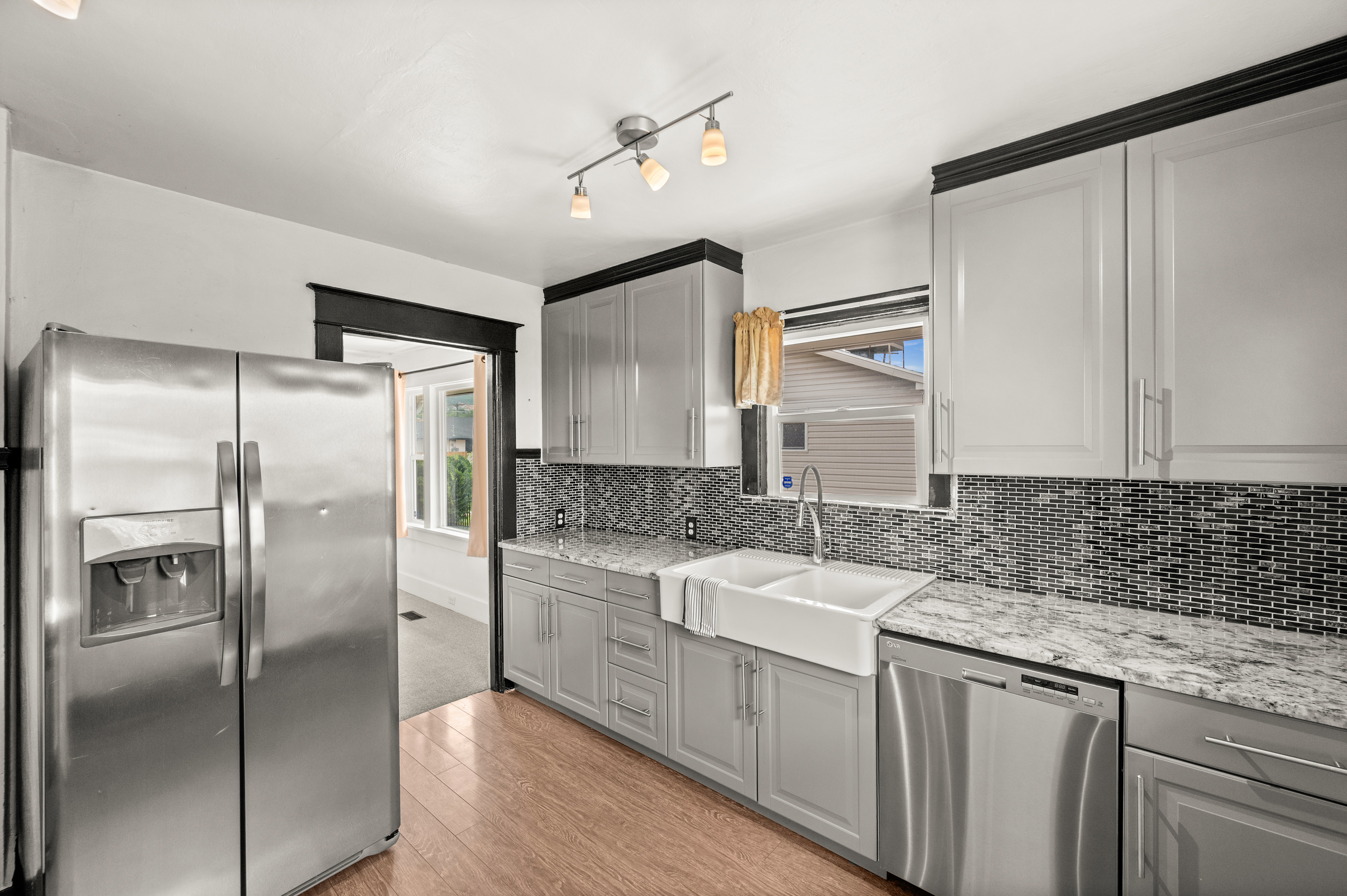 Kitchen featuring light gray cabinetry, a double farmhouse sink, granite-style countertops, mosaic tile backsplash, and wood-finish flooring
