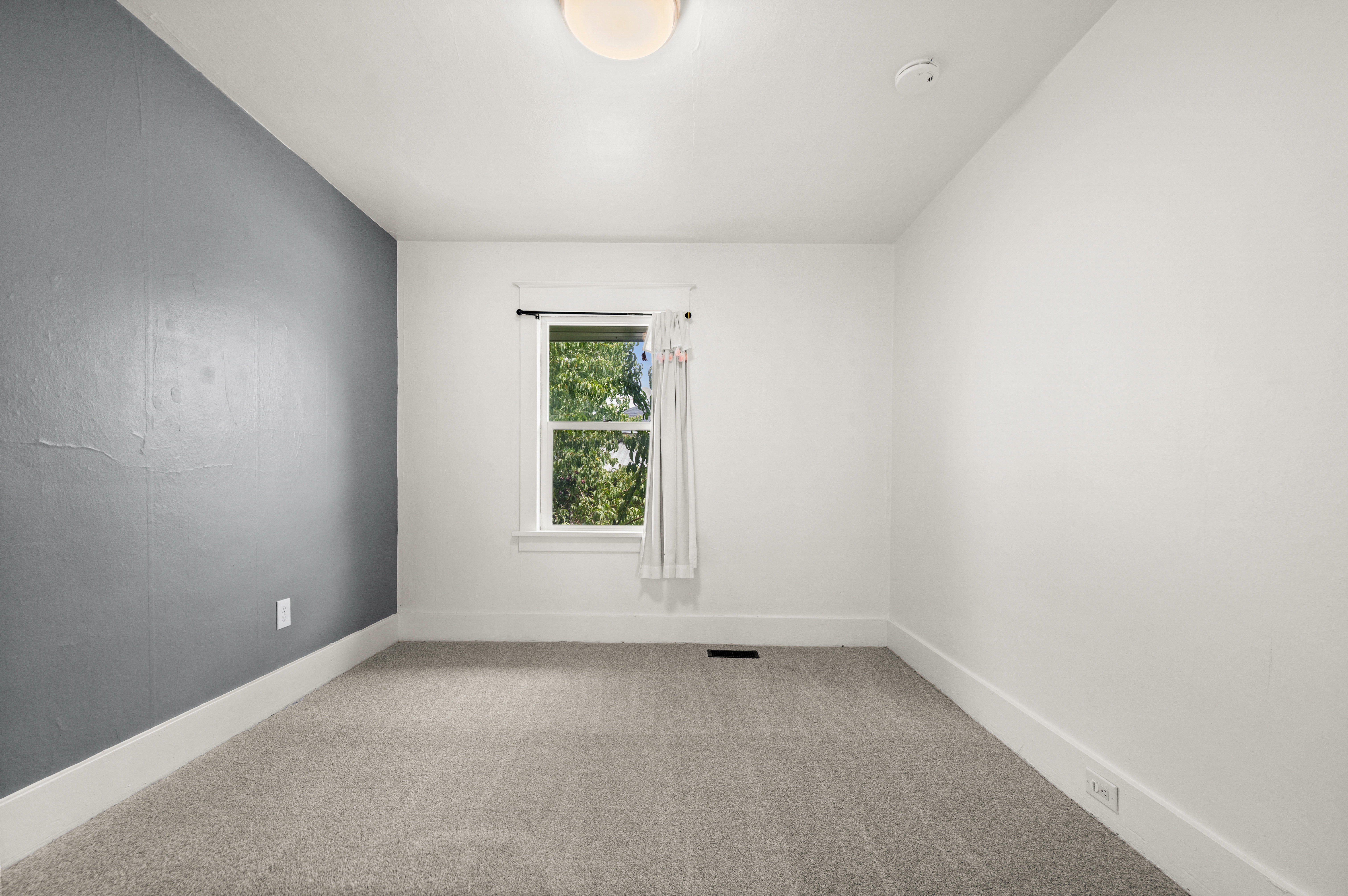 Carpeted room featuring a single window, a contrasting accent wall, white baseboards, and a ceiling-mounted light fixture