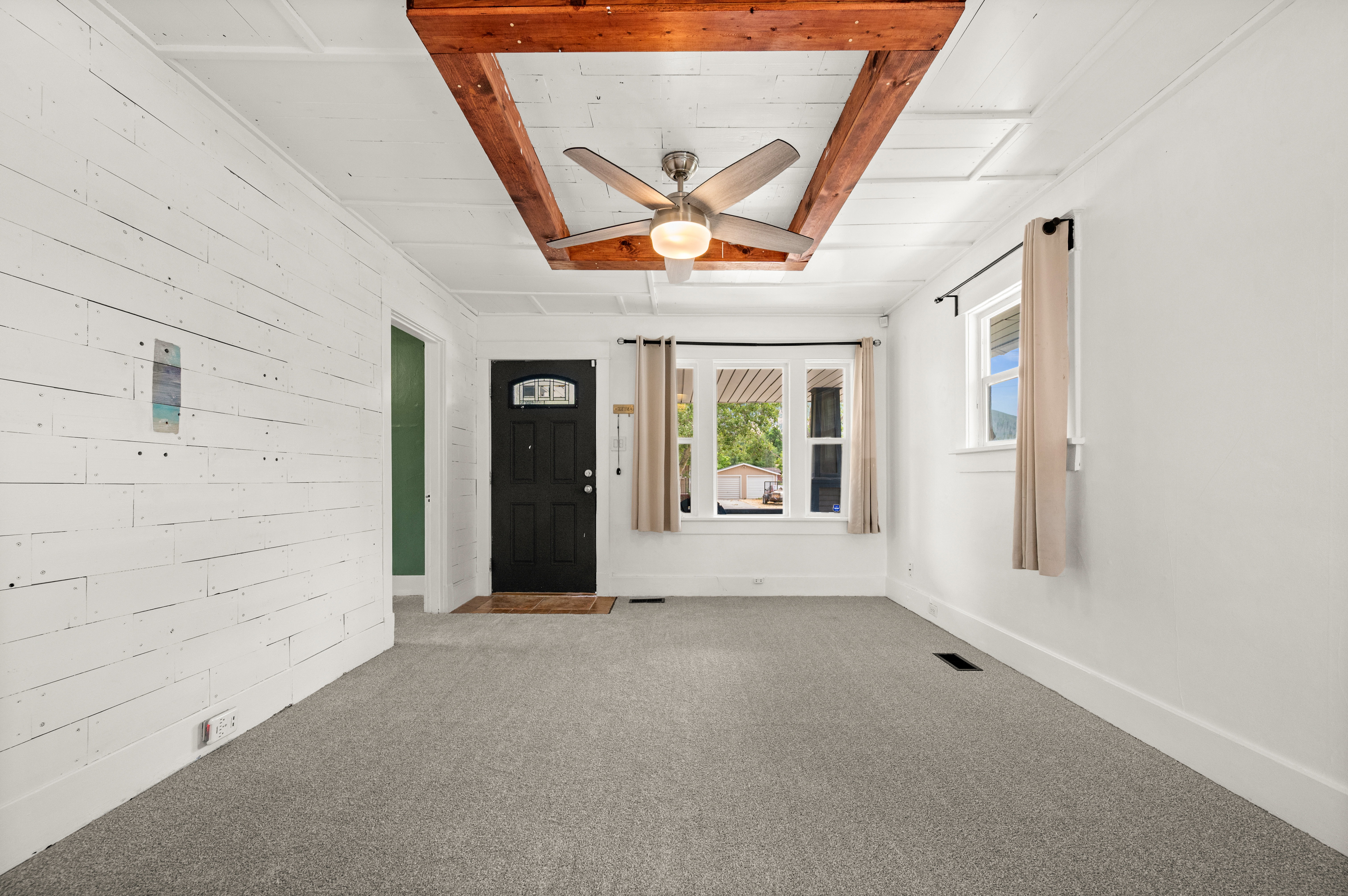 Open-concept living space featuring a wood-beam ceiling accent, a contemporary ceiling fan with integrated lighting, and light gray carpeting