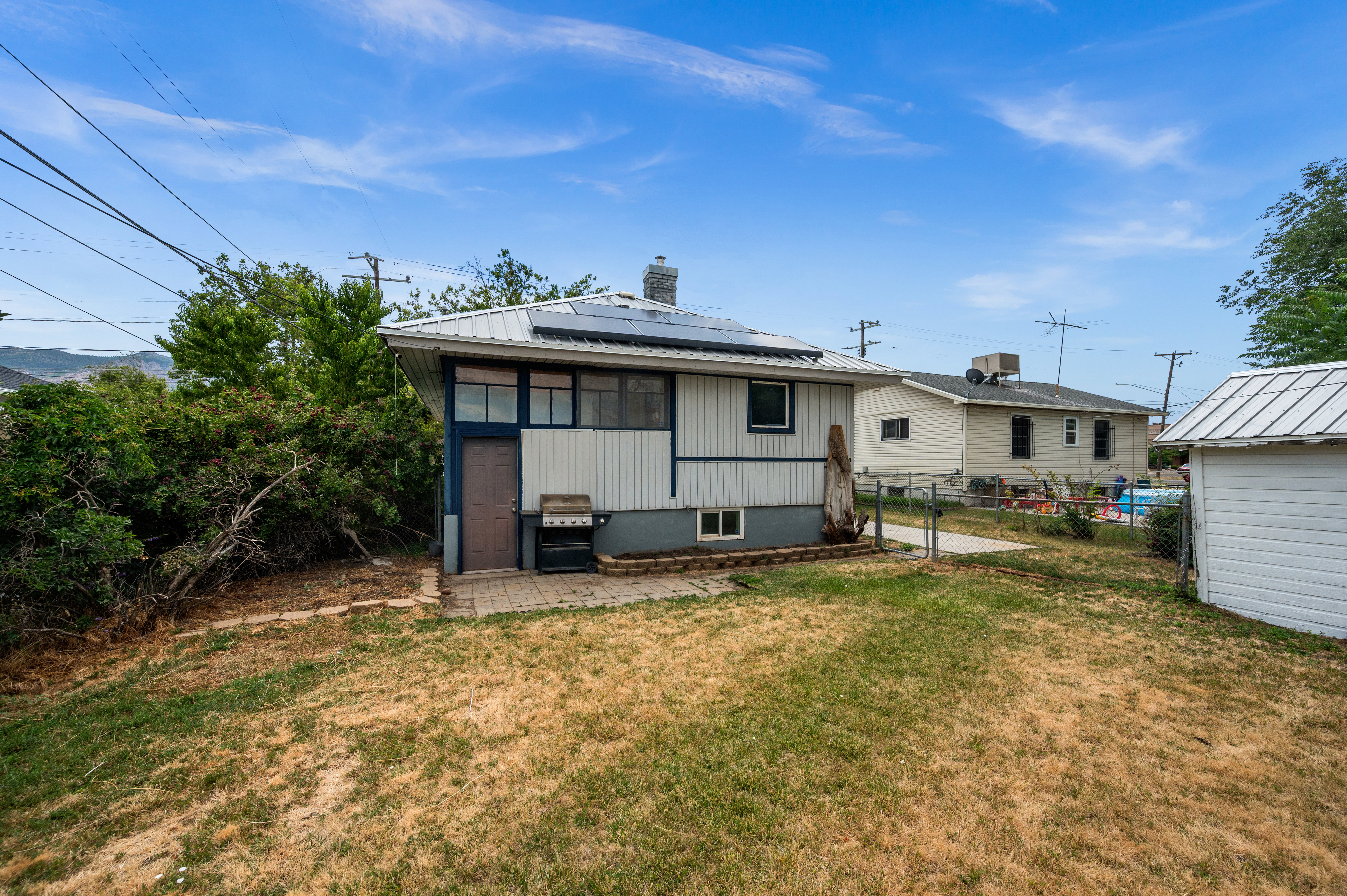Rear exterior featuring solar panels, a metal roof, and a ground-level patio area