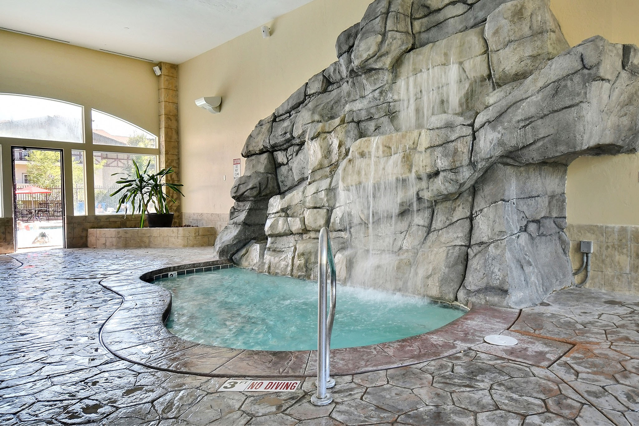Indoor spa with rock-feature waterfall, natural stone-look flooring, and a large arched window