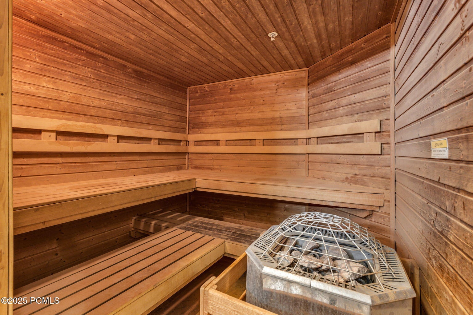 Dedicated sauna room featuring extensive wood paneling, multi-tiered wood bench seating, and an integrated sauna heater with stones