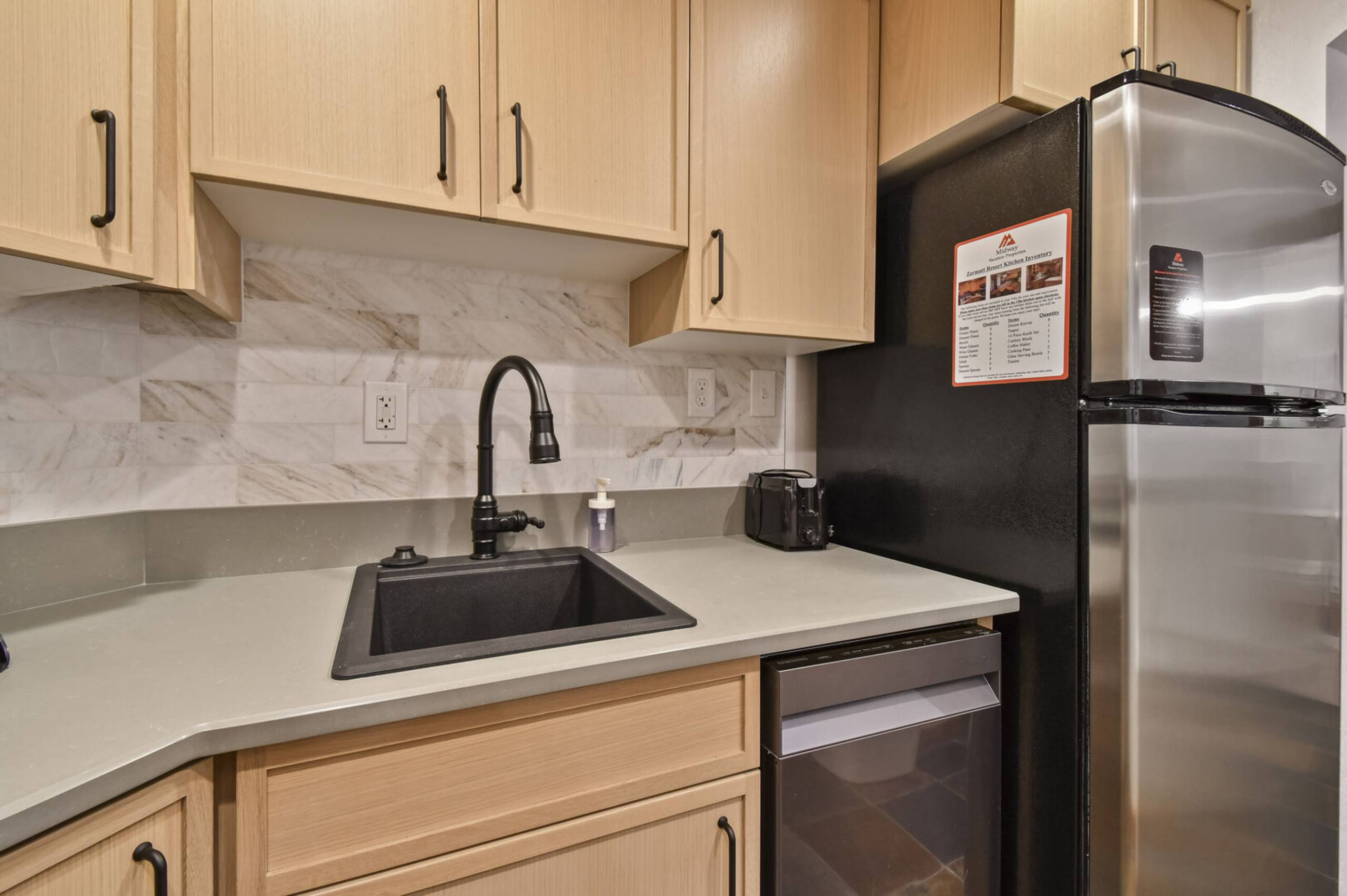 Kitchen featuring light wood cabinetry with dark hardware, a stone-finish countertop, subway tile backsplash, and a black sink with a matte black pull-down faucet