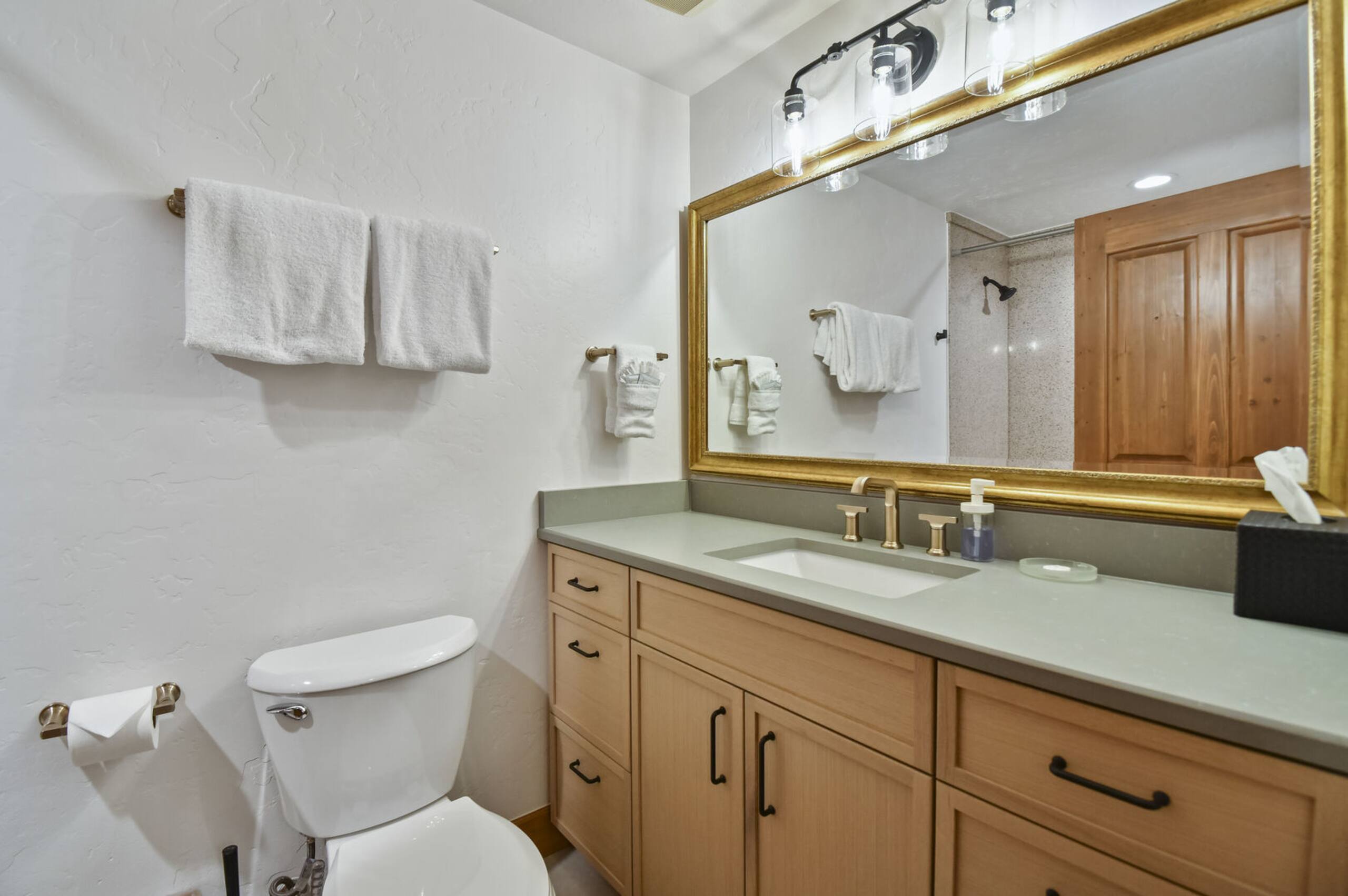 Bathroom vanity featuring light wood-finish cabinetry, a solid surface countertop, and a rectangular undermount sink with a brushed gold-tone faucet