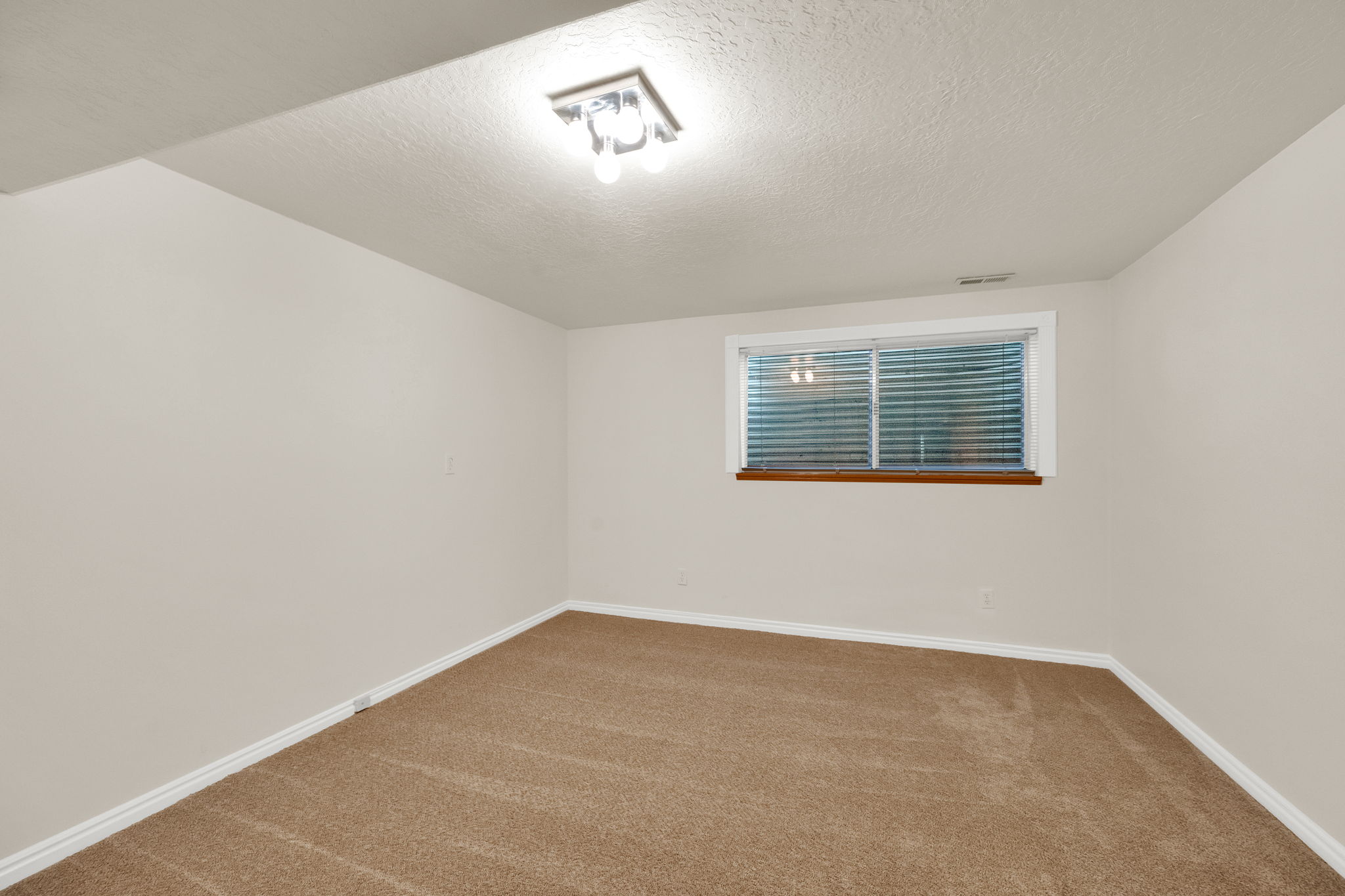 Neutral tone walls framing a carpeted room featuring a window with horizontal blinds and a wood sill