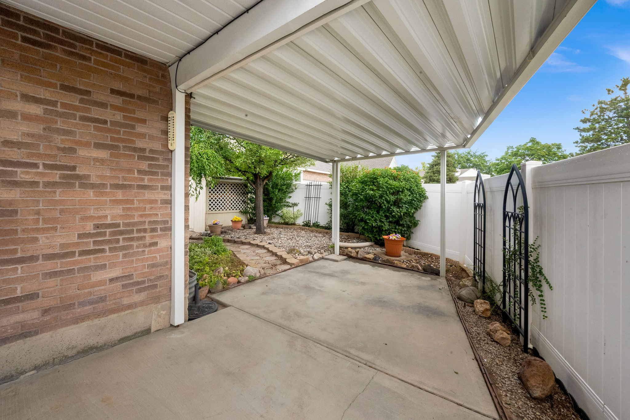 Covered patio with concrete flooring, supported by white posts, leading to an exterior garden space