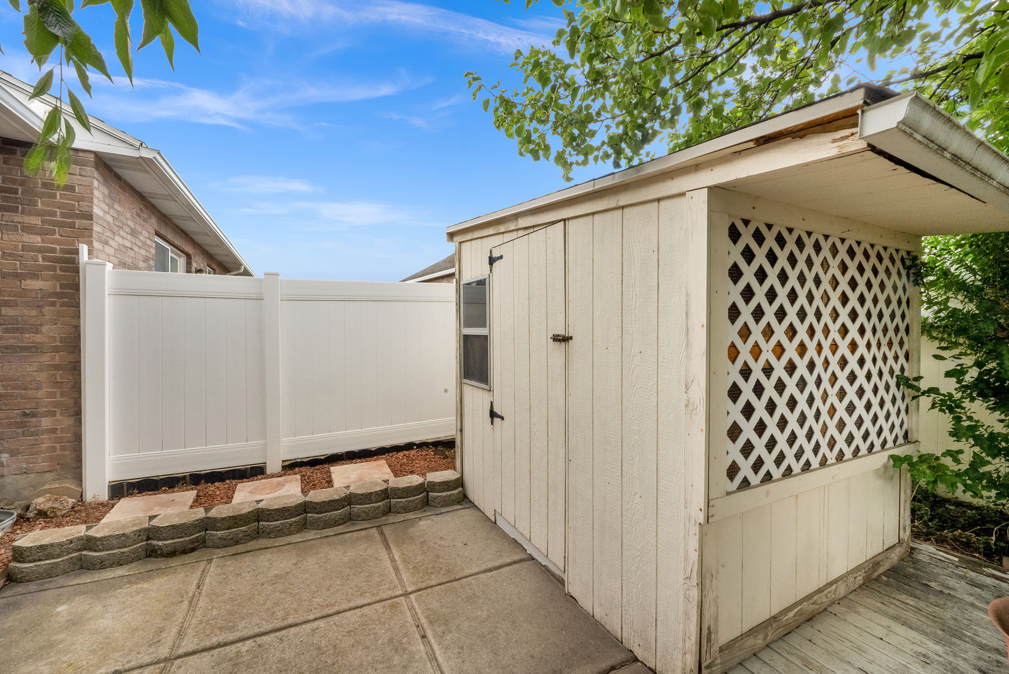 Outdoor storage shed with lattice detail and a side entrance, situated on a concrete patio