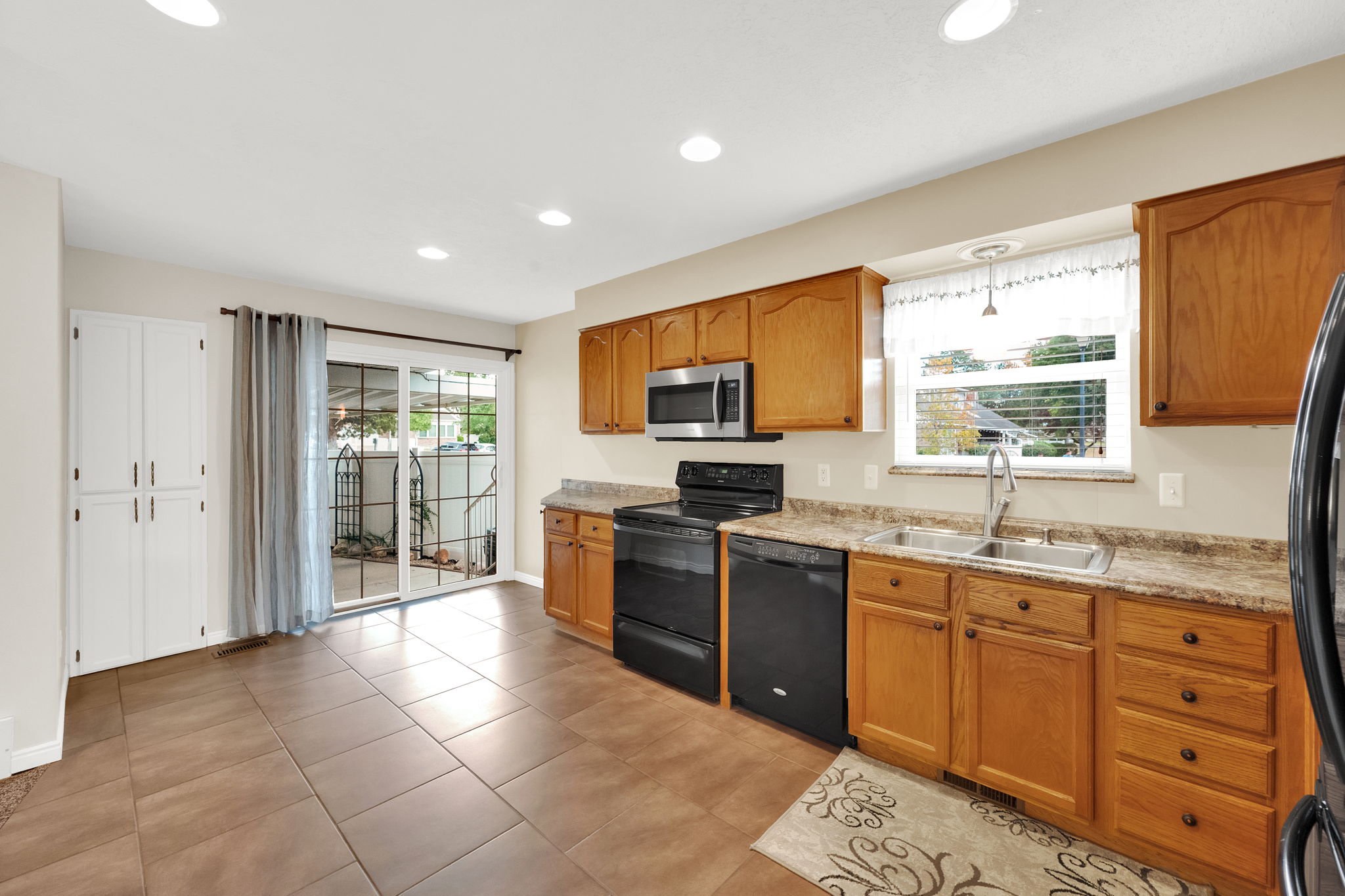 Kitchen featuring wood cabinetry, stainless steel microwave, black appliances, double basin sink, and tile flooring
