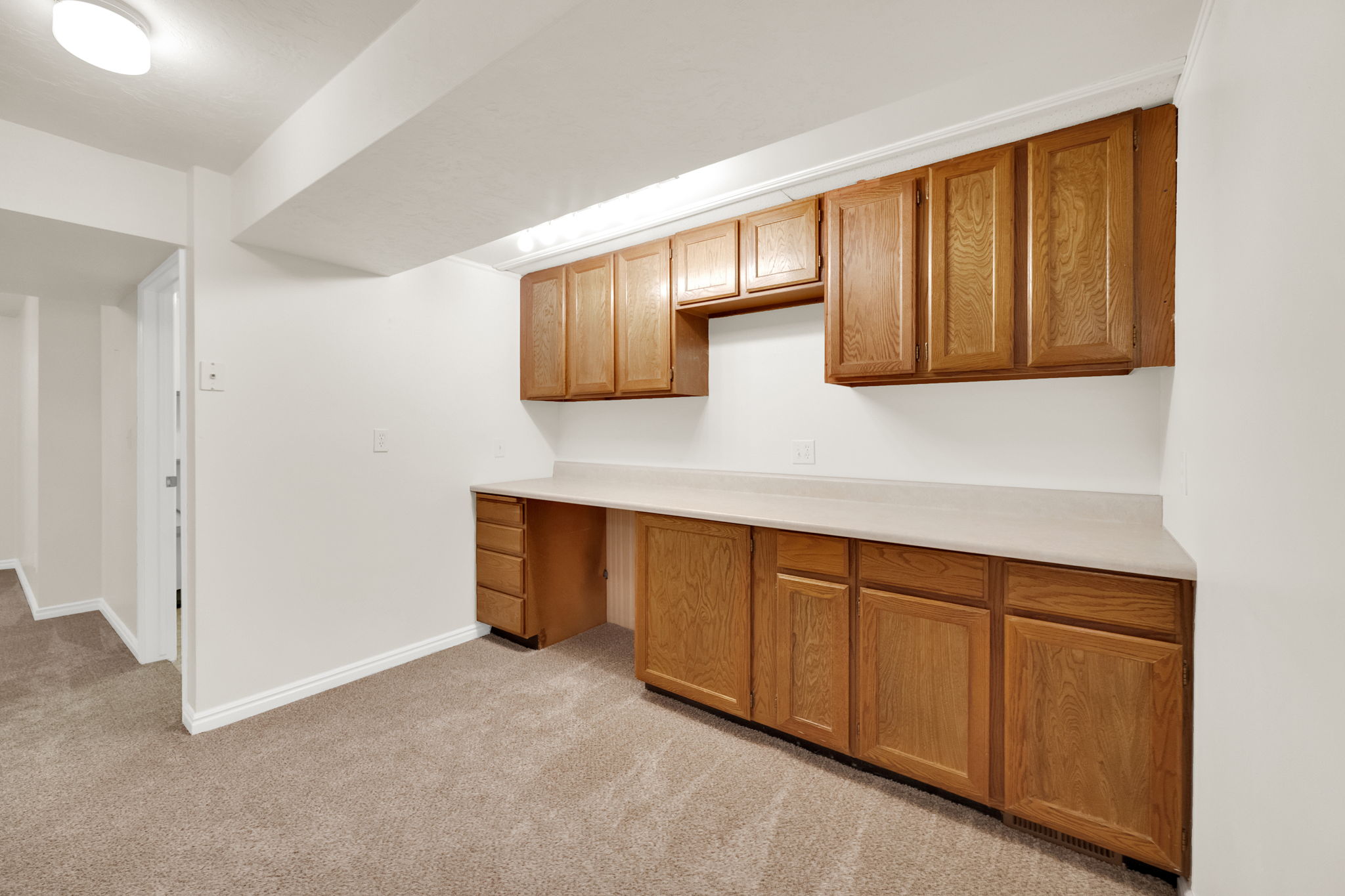 Built-in desk area featuring light wood-finish cabinetry, a neutral countertop, and overhead lighting