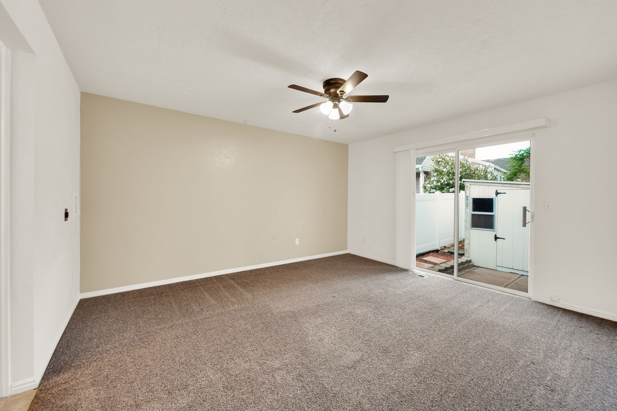Carpeted interior space featuring a ceiling fan with integrated lighting, a sliding glass door, and white baseboards