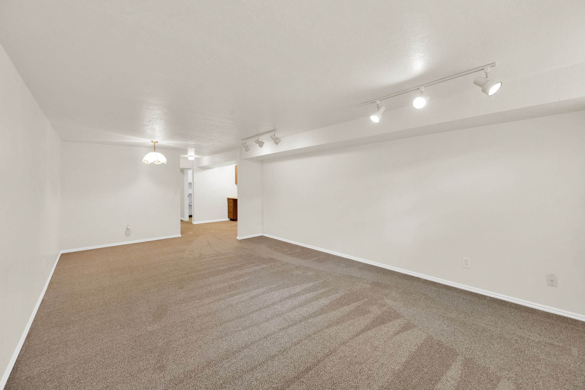 Spacious room with neutral-toned carpeting, white walls, and bright overhead lighting