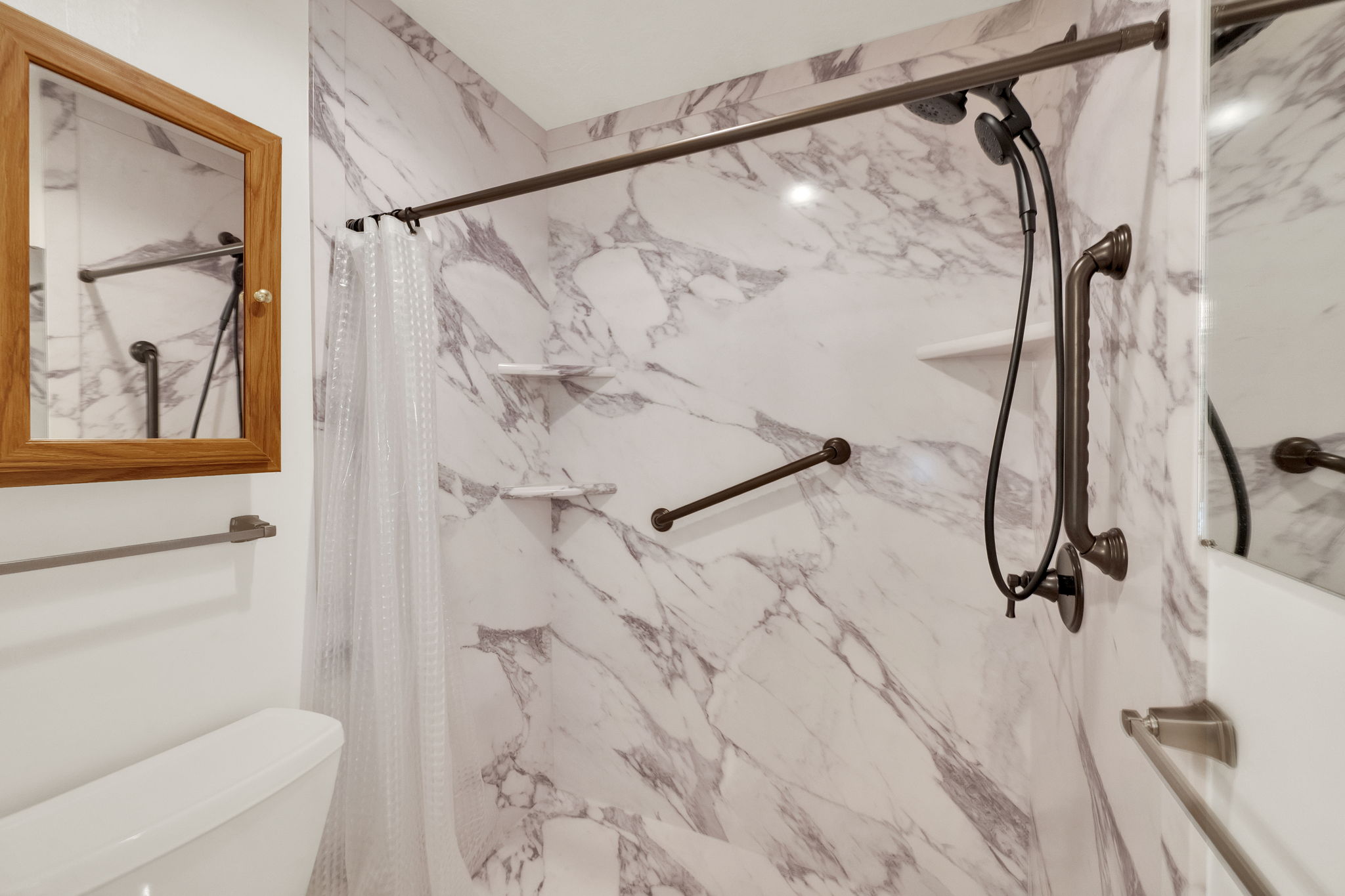 Shower stall featuring marble-patterned paneling, a bronze-finish shower bar, and a handheld showerhead