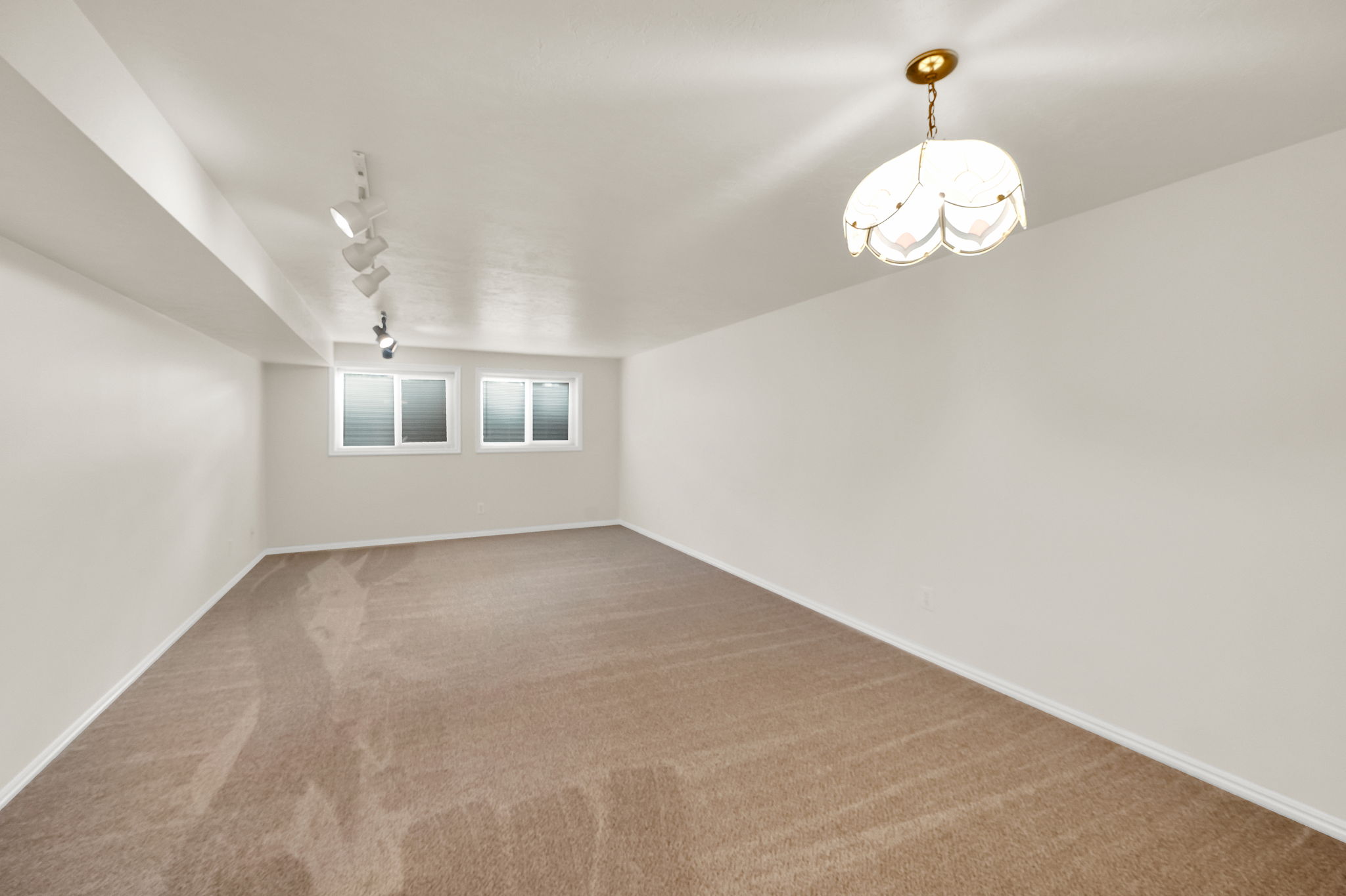 Carpeted room featuring two transom windows, track lighting, and a decorative ceiling fixture