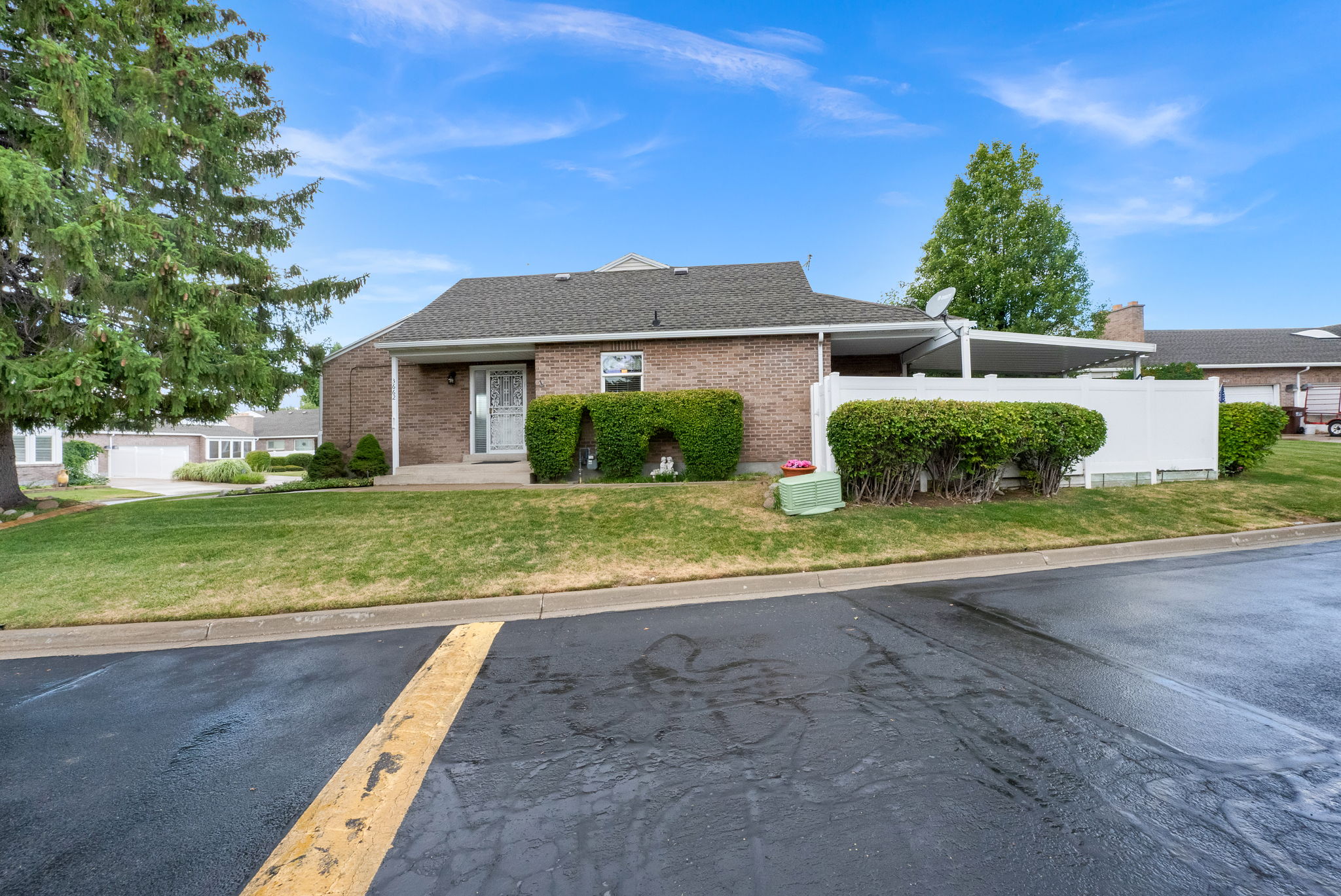 Brick exterior property featuring a covered entry, mature landscaping, and a white privacy fence