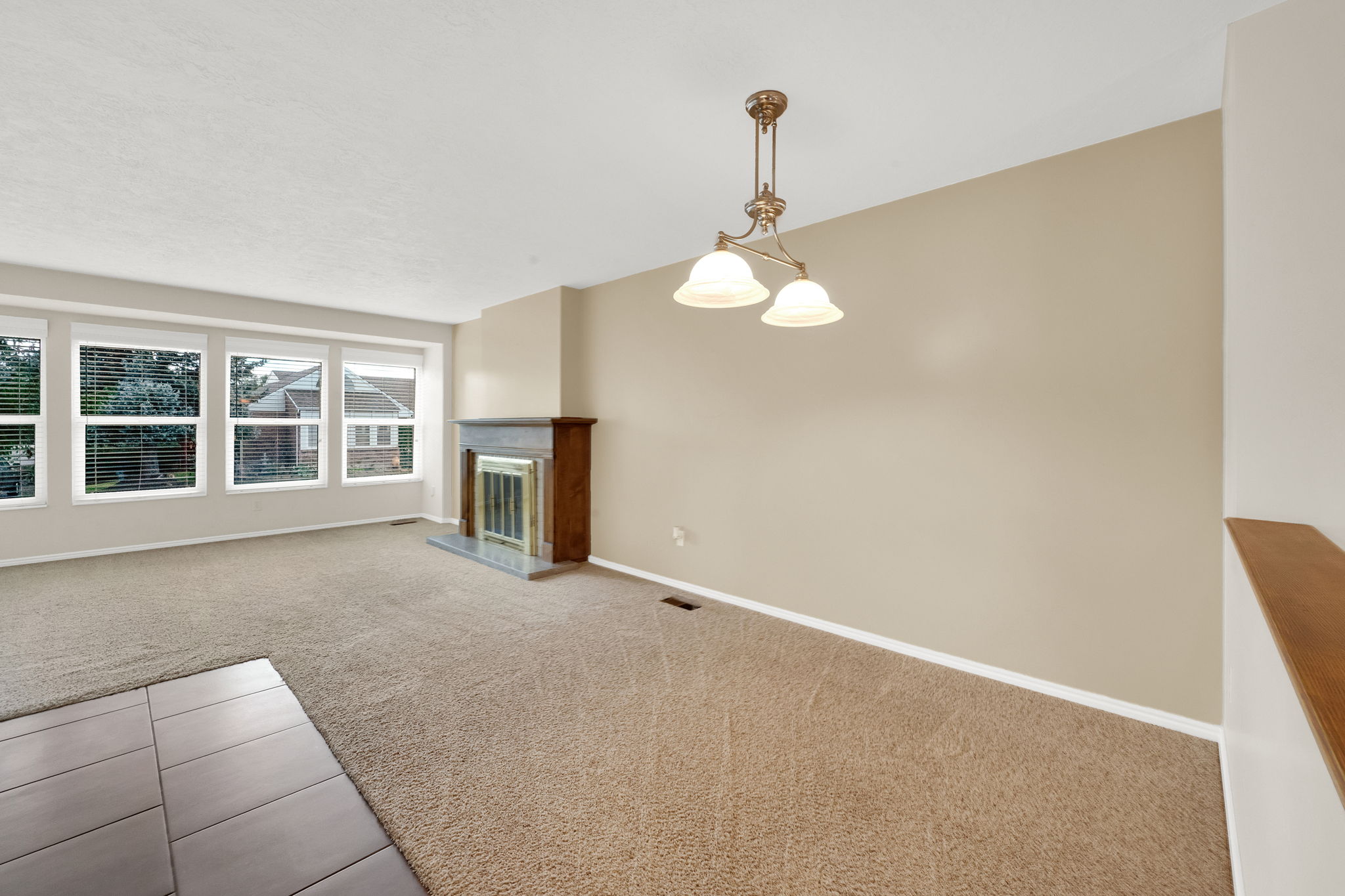 Living space featuring a fireplace with a wood mantle and stone surround, broad wall-to-wall carpeting, multiple large windows, and a classic ceiling light fixture