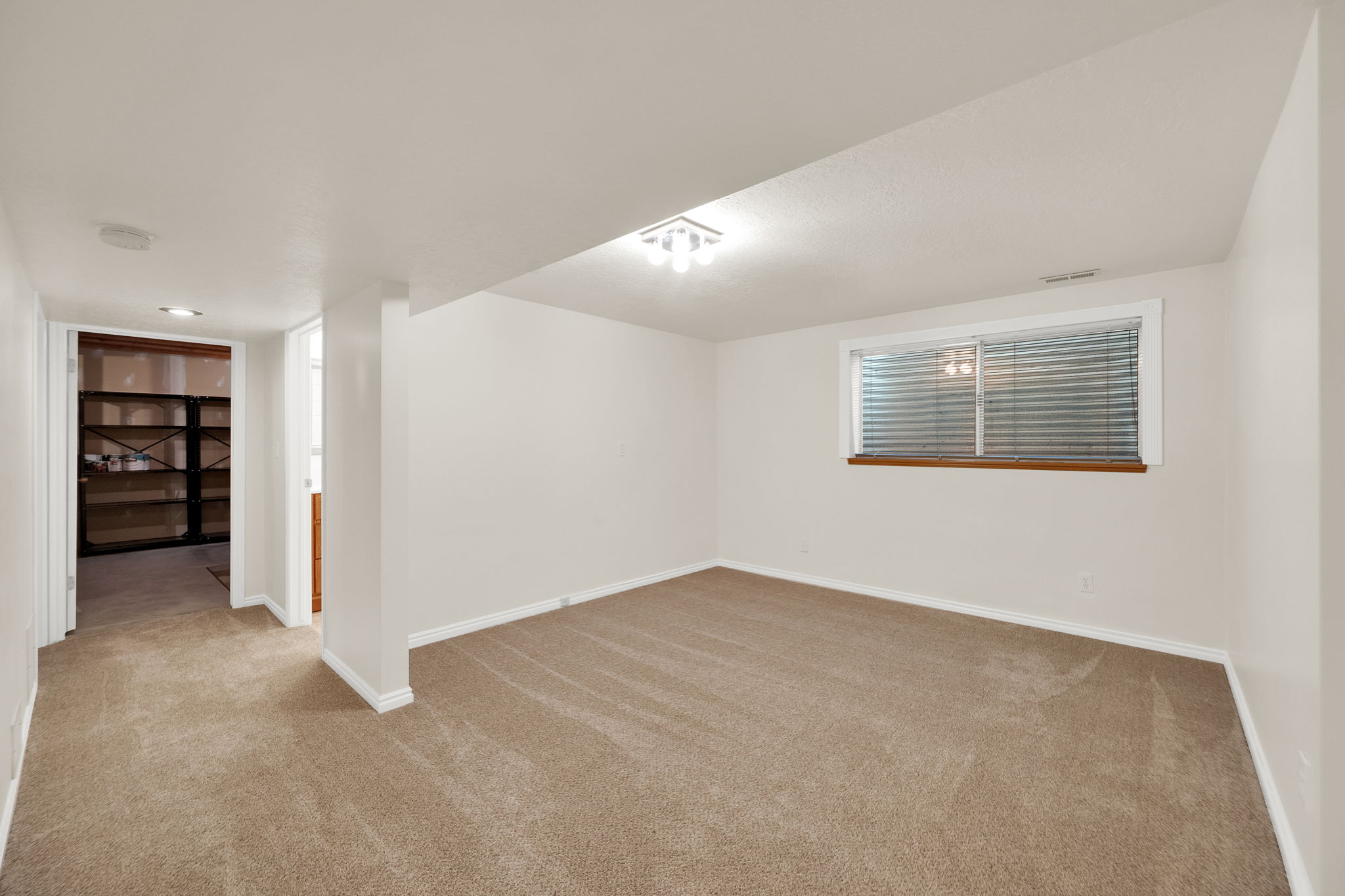 Carpeted interior space featuring a window with horizontal blinds, a wood-finish window sill, and white baseboards