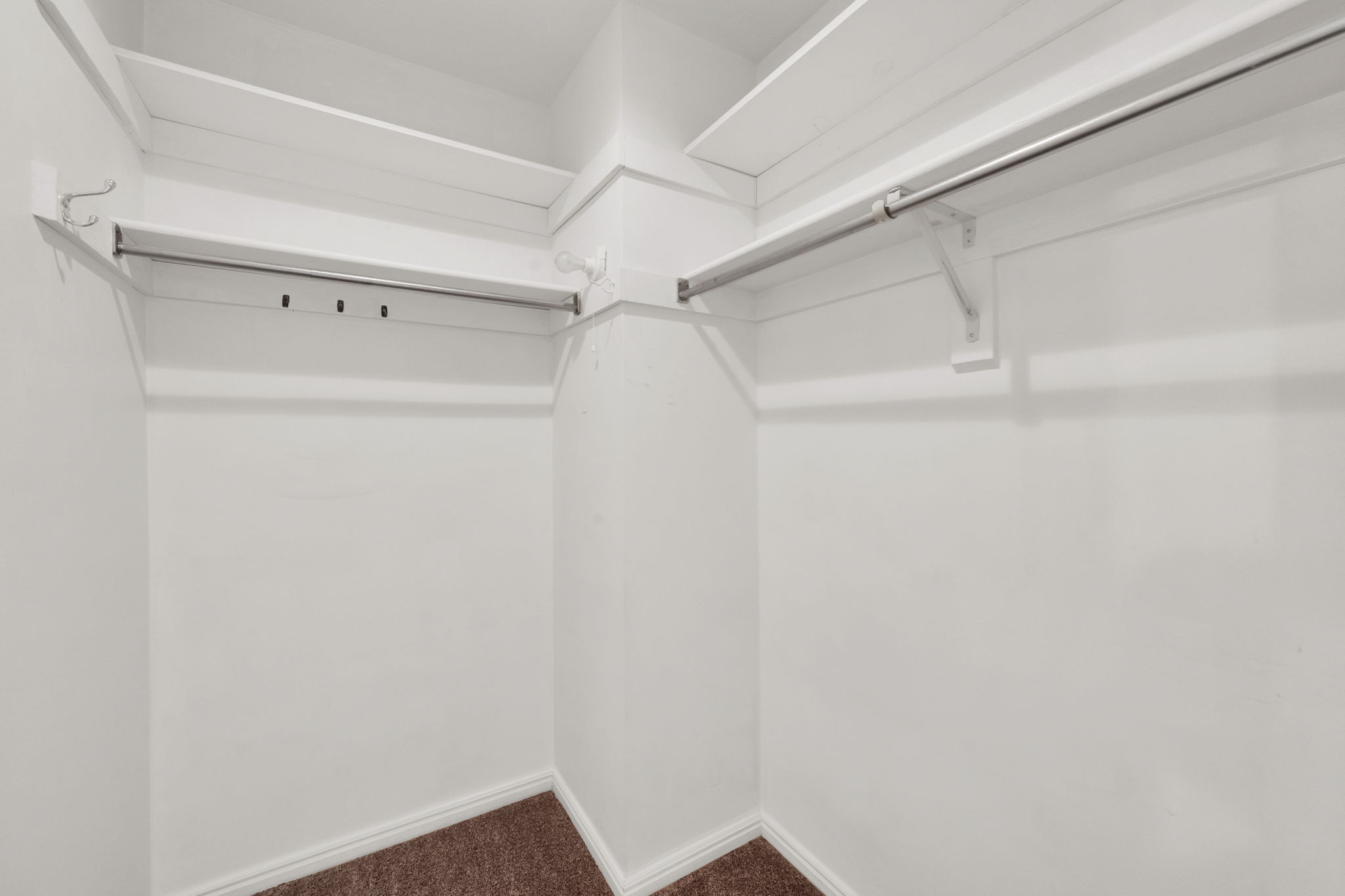 Walk-in closet with white walls, upper shelving, and two clothing rods