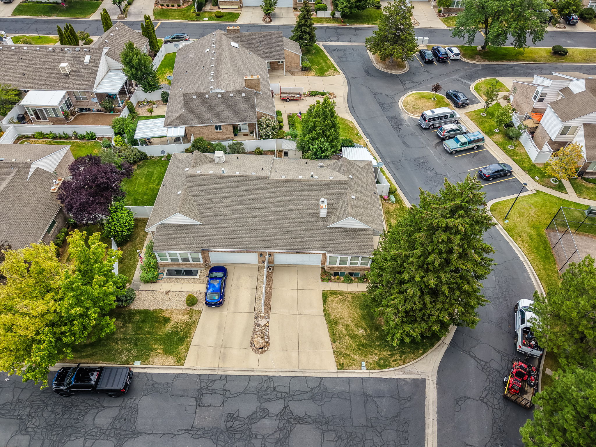 Residential property featuring a concrete driveway, attached two-car garage, mature landscaping, a sloped roofline, and a paved street frontage