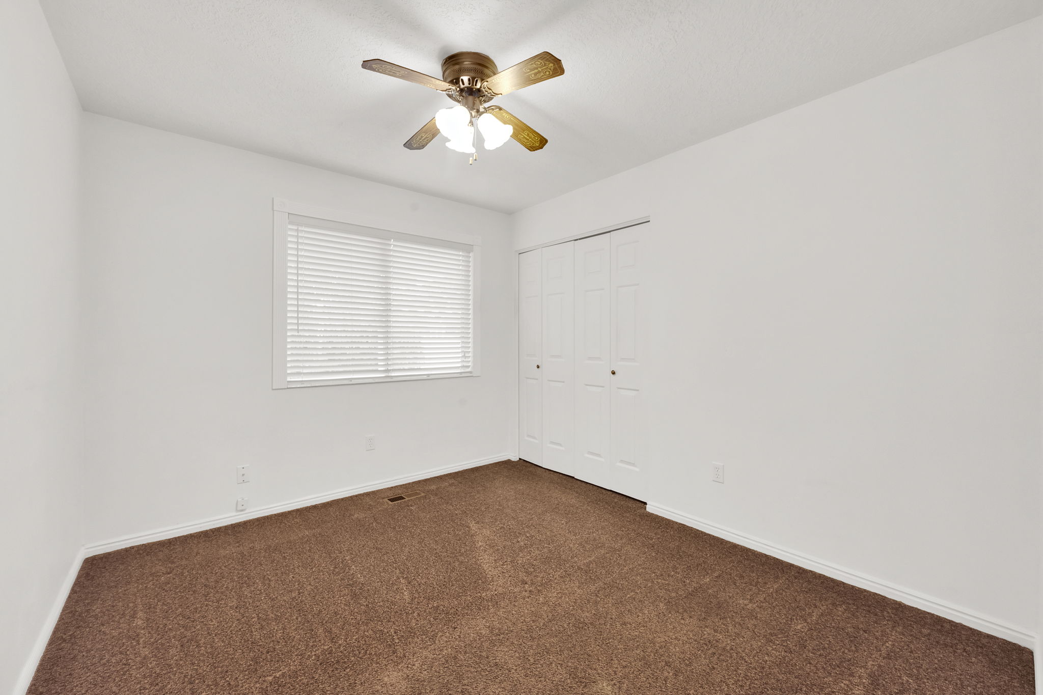 Bedroom featuring neutral wall paint, brown carpet, window with blinds, and bi-fold closet doors