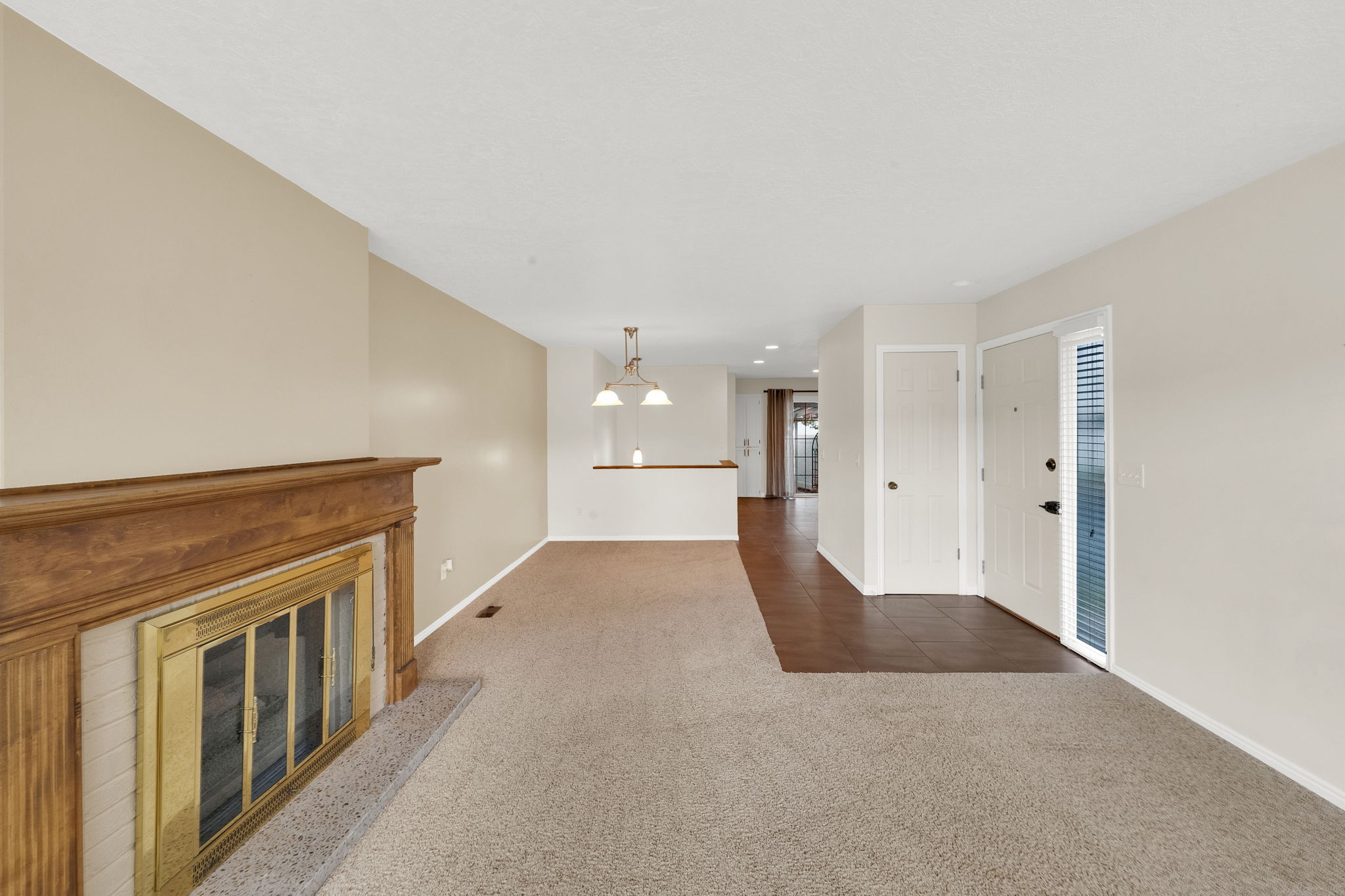 Living area featuring a wood-mantled fireplace with a brass firebox, light-toned carpeting, and neutral wall tones