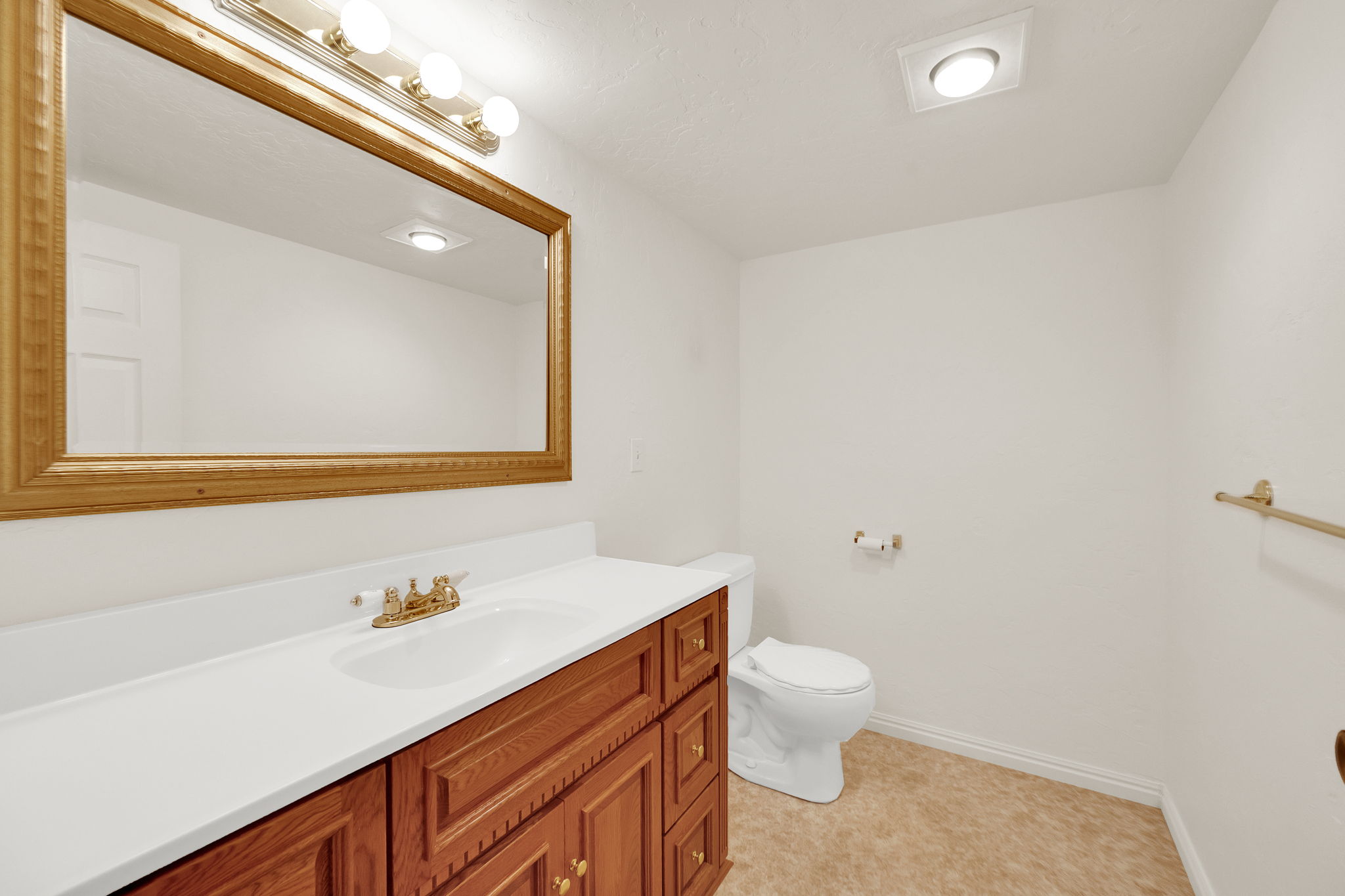 Bathroom featuring a vanity with a white countertop and wood-finish cabinetry, a large framed mirror, and a toilet