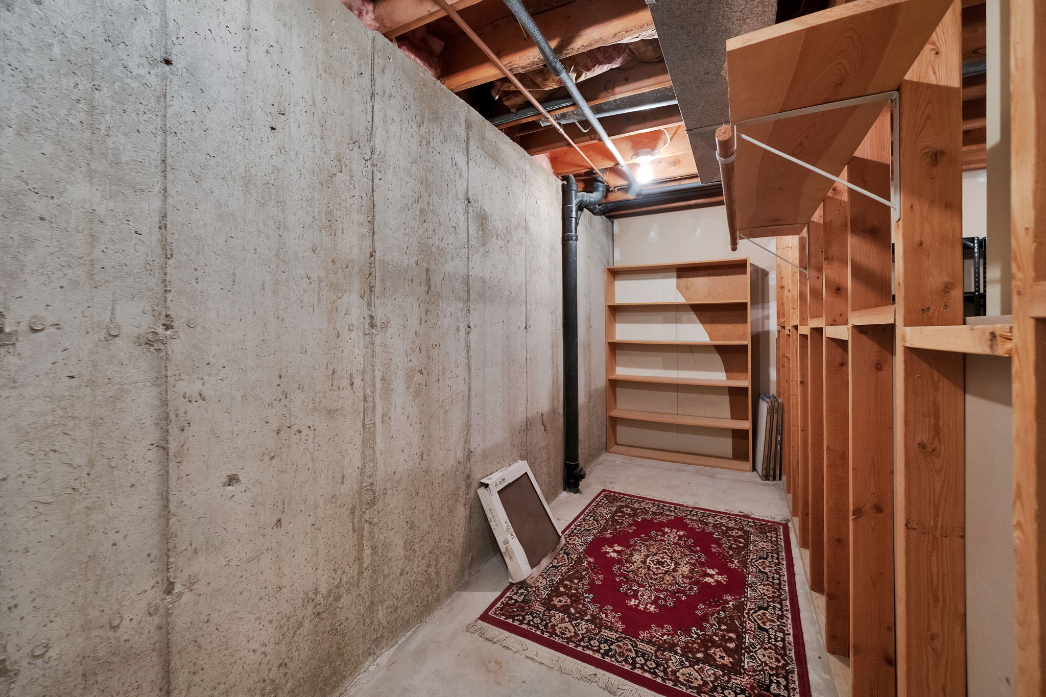 Unfinished basement area featuring exposed concrete walls and ceiling joists